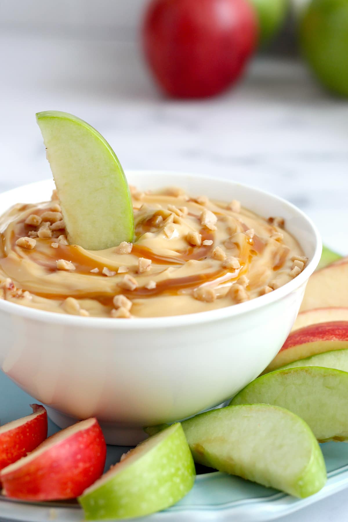 Creamy caramel apple dip in a white ceramic bowl drizzled with caramel and topped with heath bits.