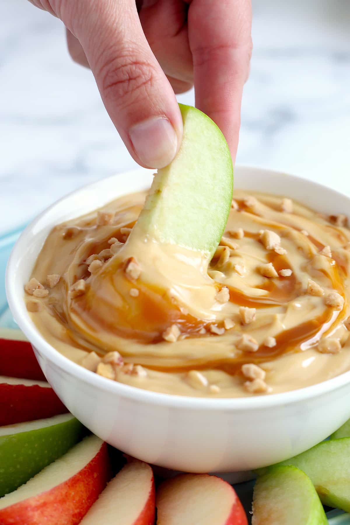 A slice of apple dipped in caramel apple dip with caramel drizzle and toffee bits.