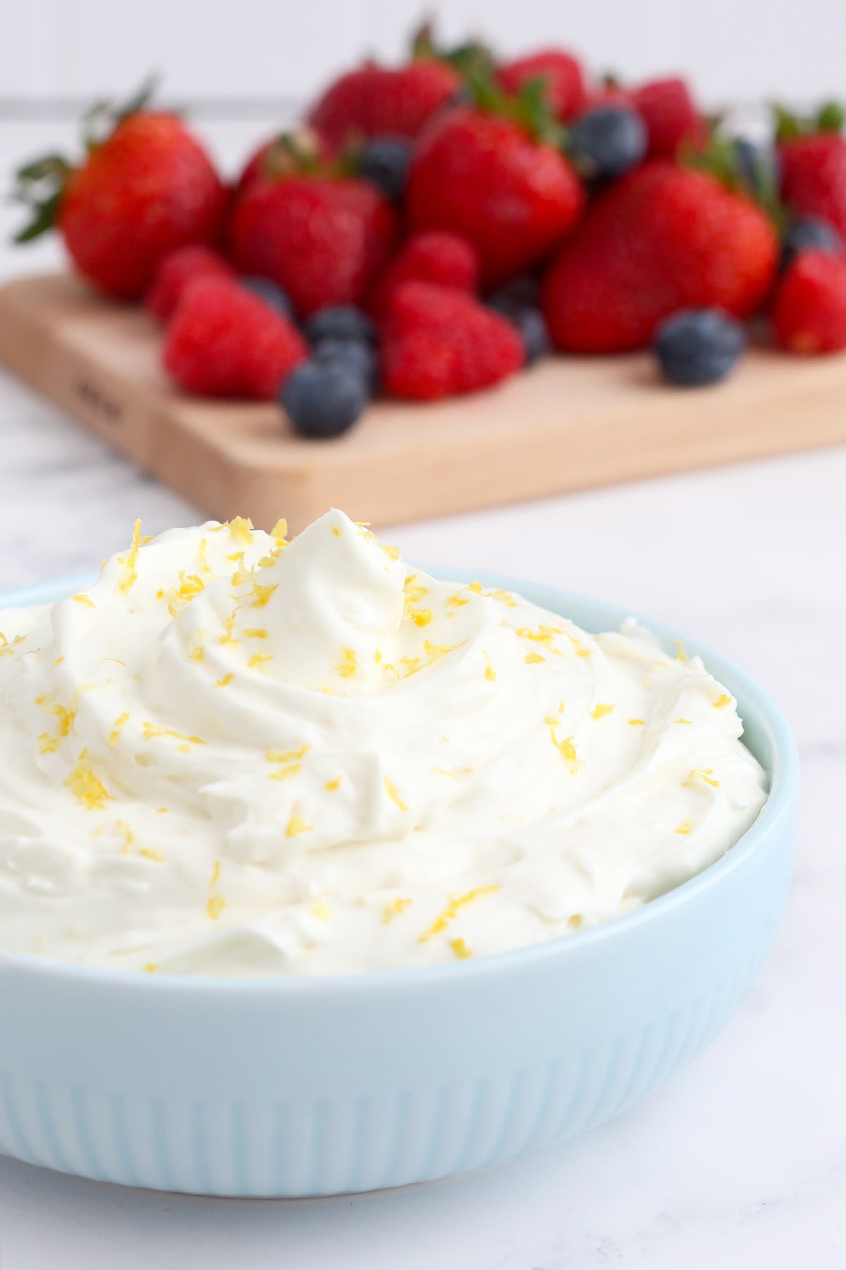 A bowl of creamy lemon fruit dip with fresh lemon zest and assorted berries.