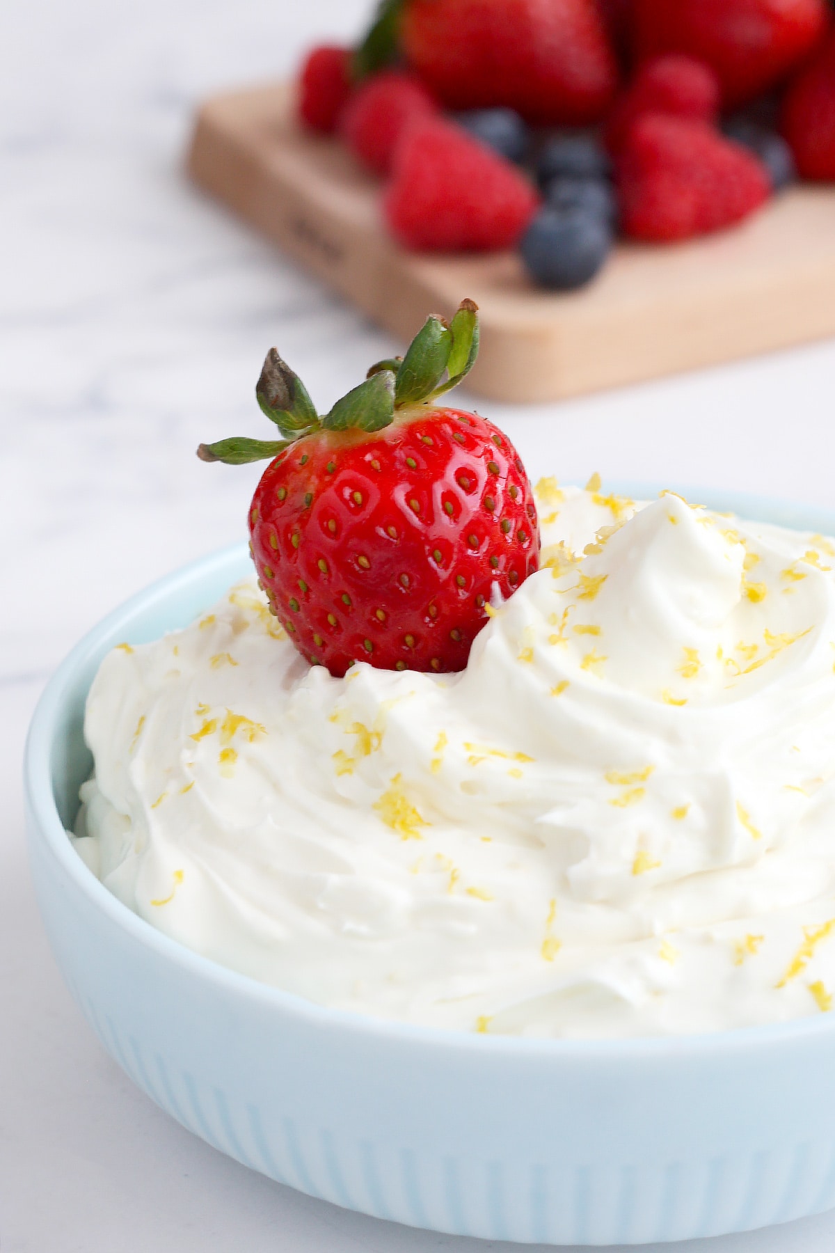 Creamy fruit dip topped with lemon zest and a fresh strawberry in a blue bowl.
