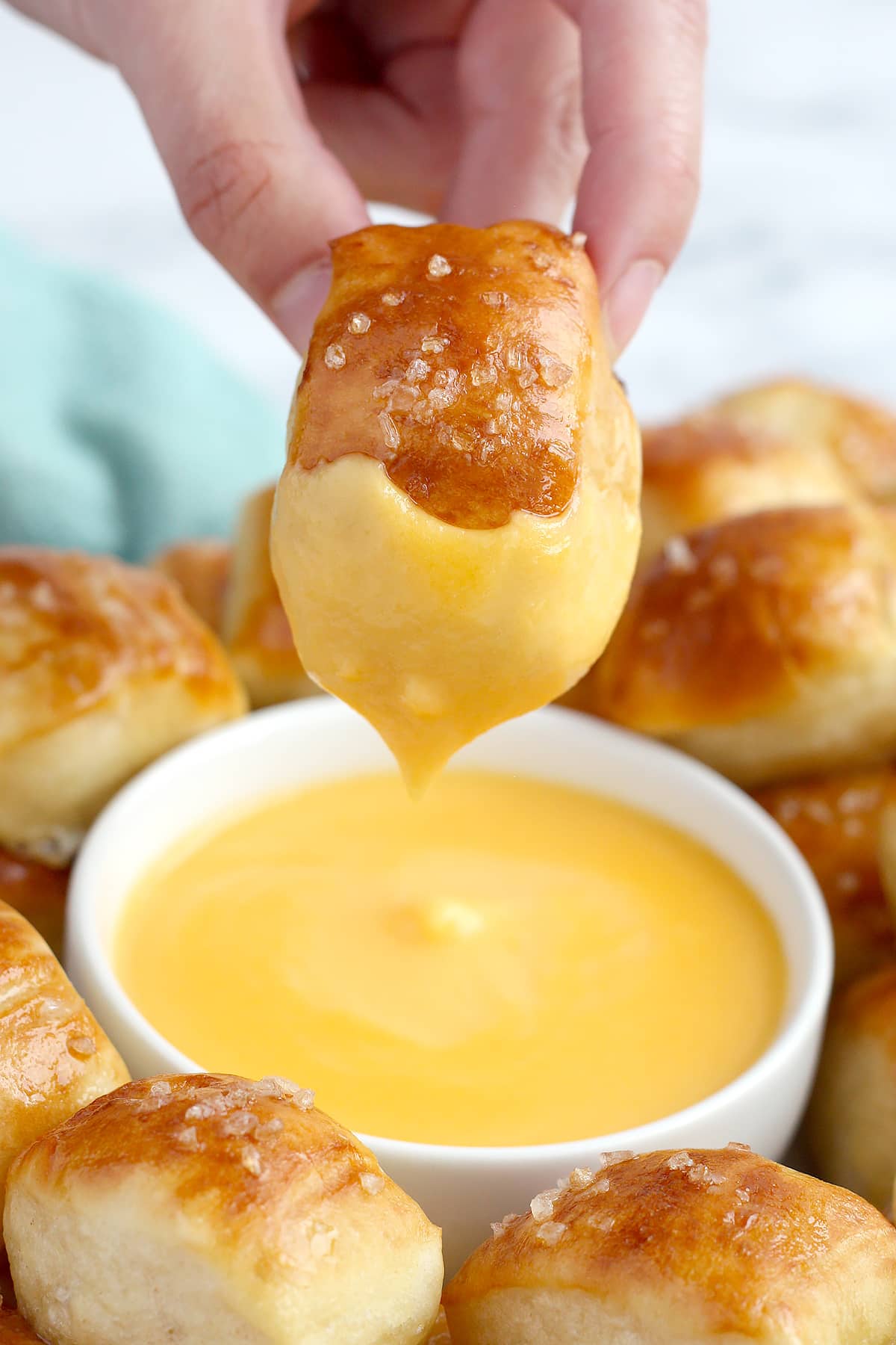 A soft pretzel bite dipped in a bowl of cheese dip.
