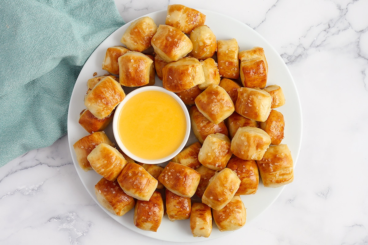 Pretzel Bites on a white plate with cheese sauce and a green linen.