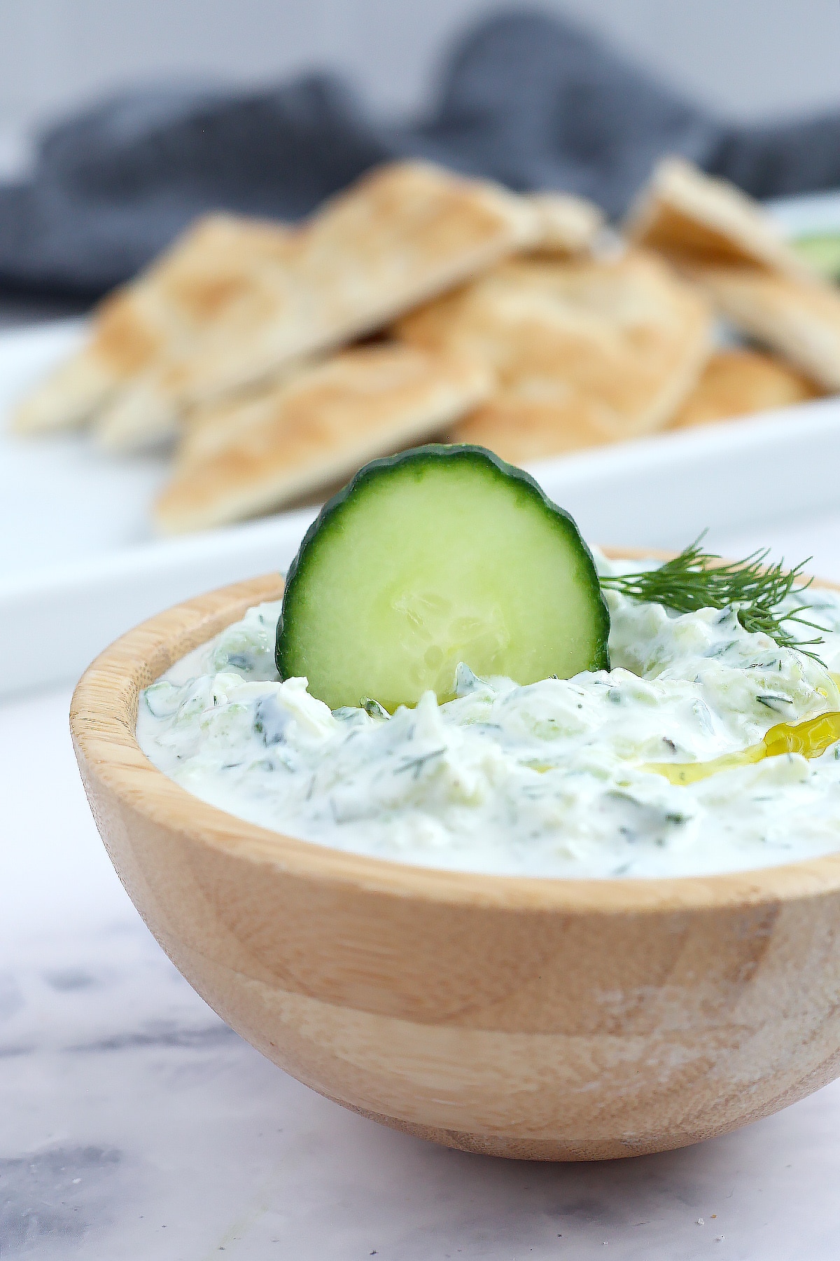 Homemade tzatziki dip in a wooden bowl served with fresh pita triangles.