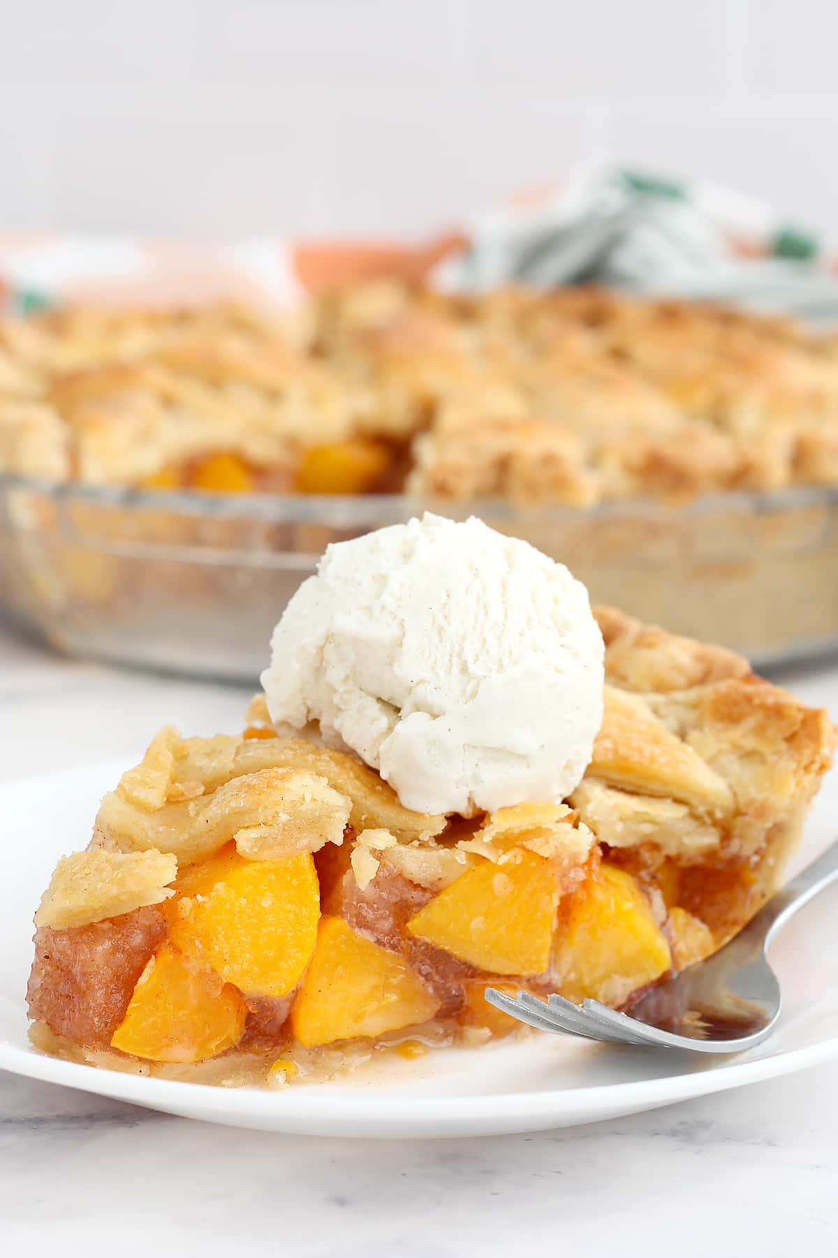 A slice of peach pie on a serving plate, topped with vanilla ice cream.