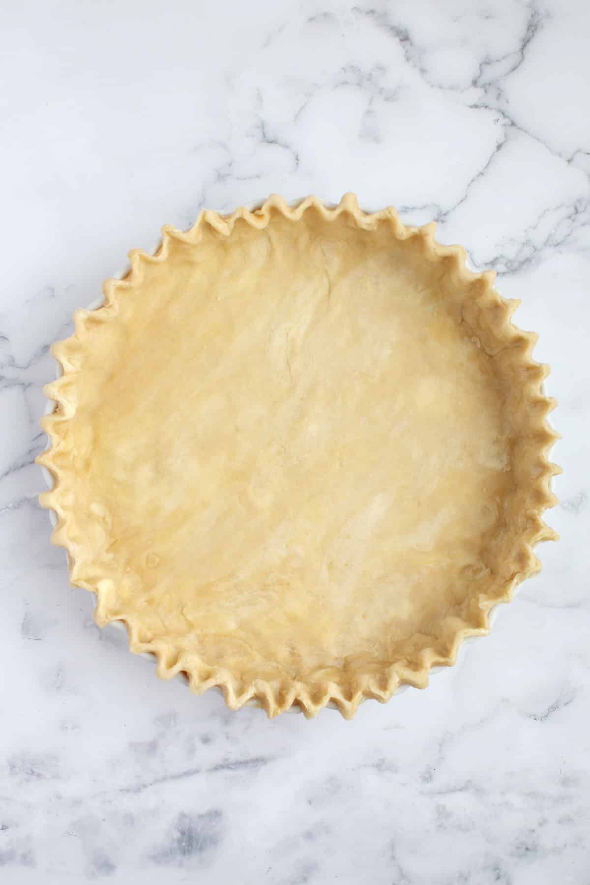 Fluted all-butter tart dough in a white tart plate.