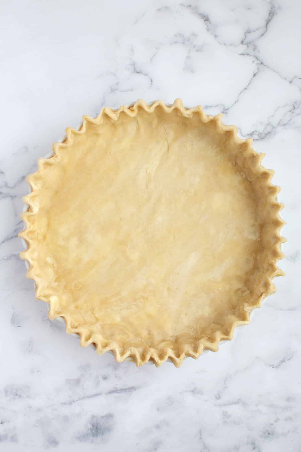 Fluted all-butter pie dough in a white pie plate.