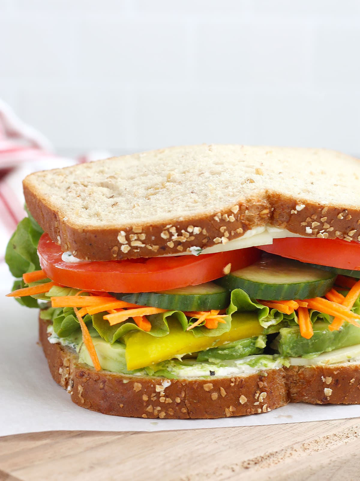 A veggie sandwich with tomatoes, cucumbers, pickles, carrots and spinach on wheat bread.