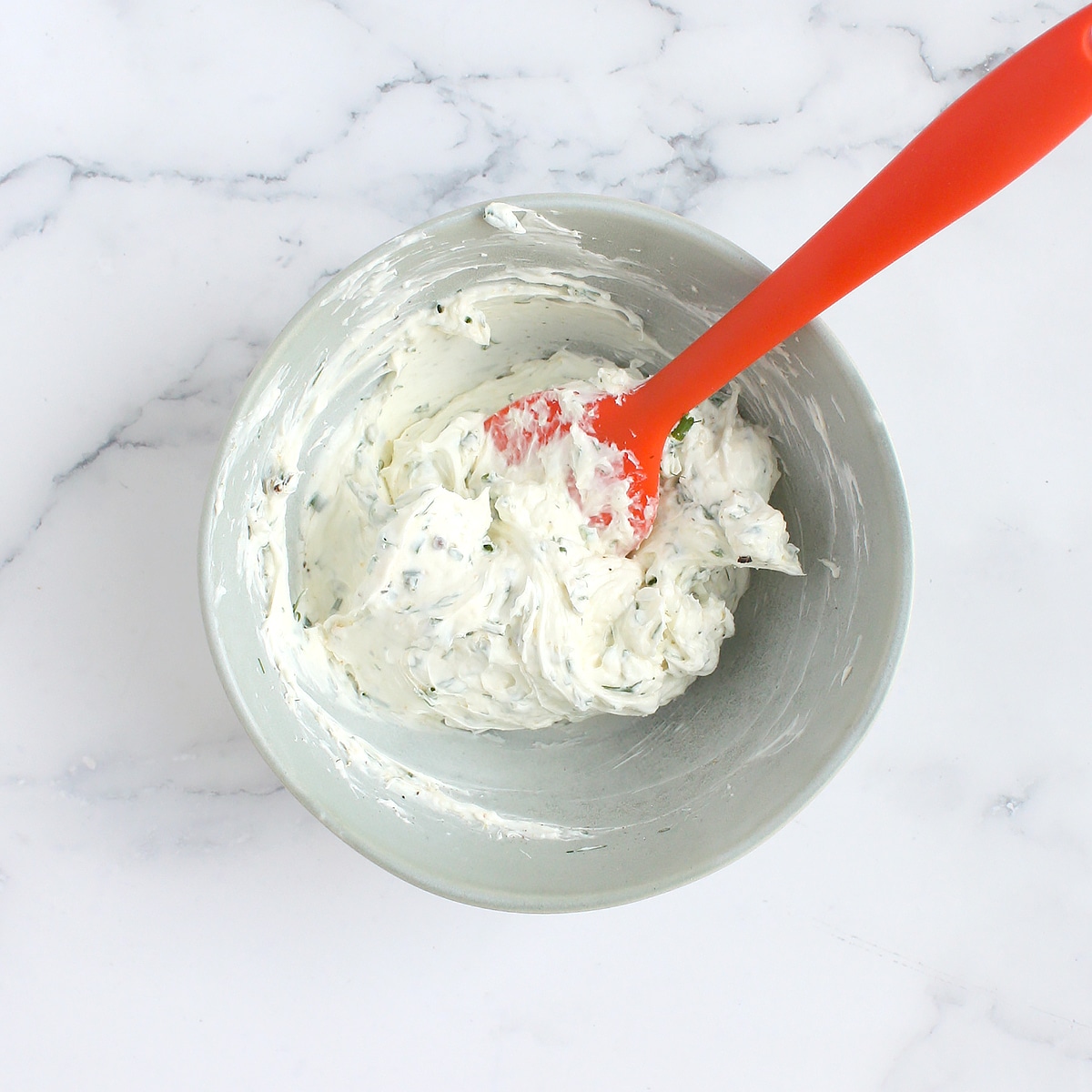 Herbed cream cheese in a bowl with a red spoon.