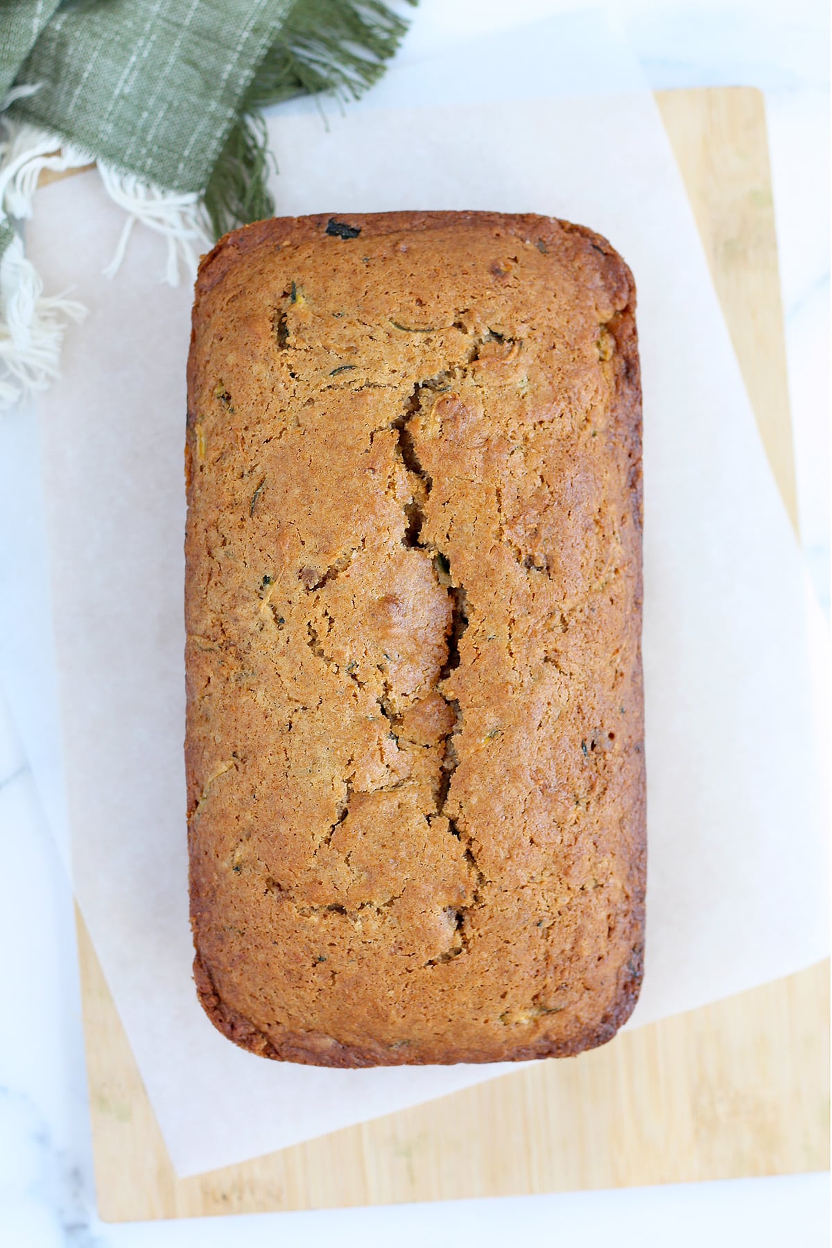 A golden brown loaf of zucchini bread on a cutting board with a green linen in the background.