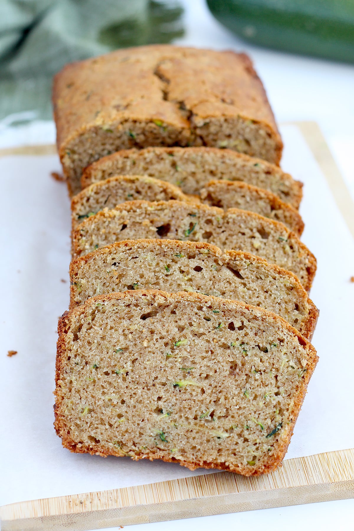 A loaf of zucchini bread, sliced on a wooden cutting board covered in parchment.