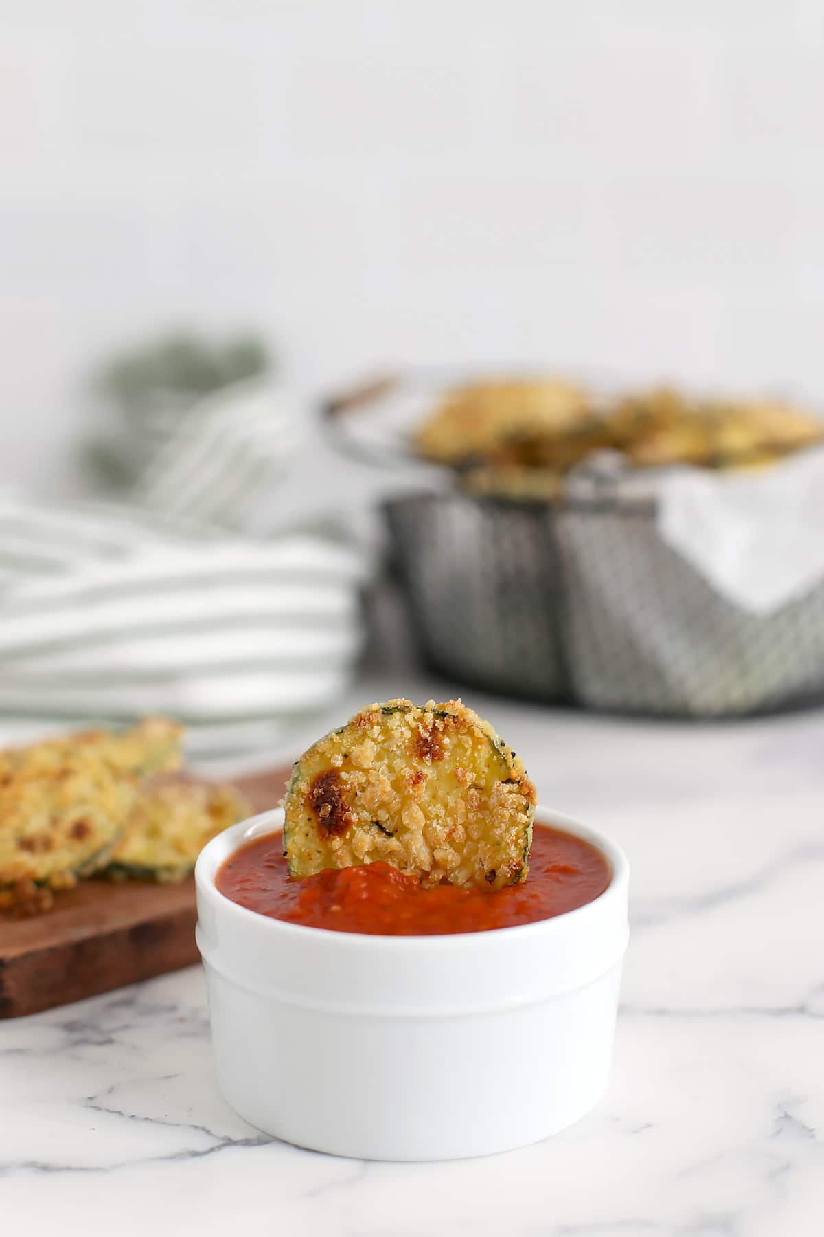 A baked zucchini chip dipped in a small bowl of marinara sauce.