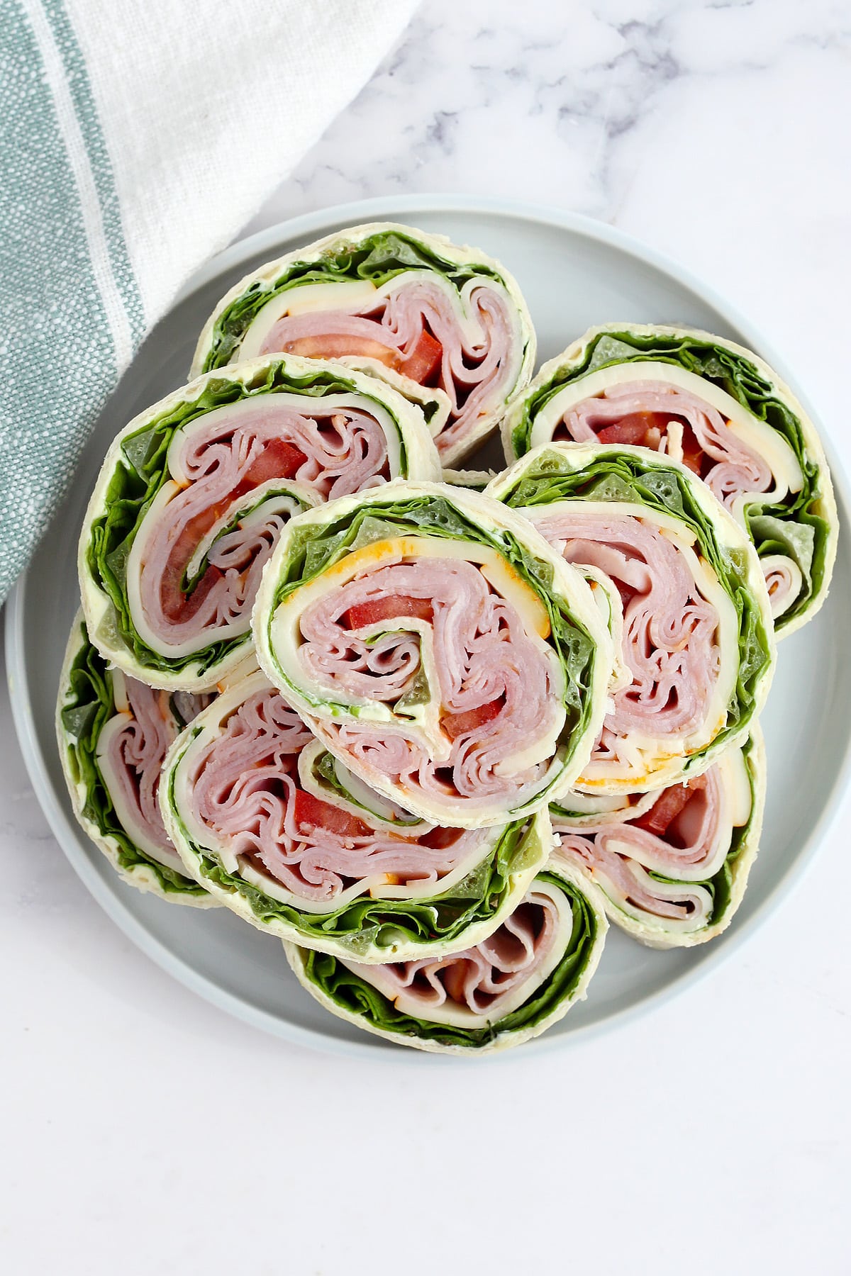 Ham and cheese pinwheels with lettuce and tomato on a grey plate.