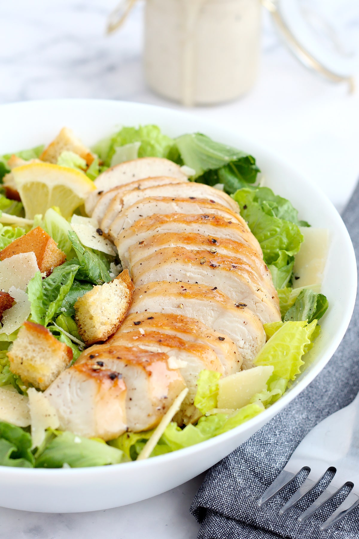 Homemade chicken caesar salad with croutons and grilled chicken in a white serving bowl.