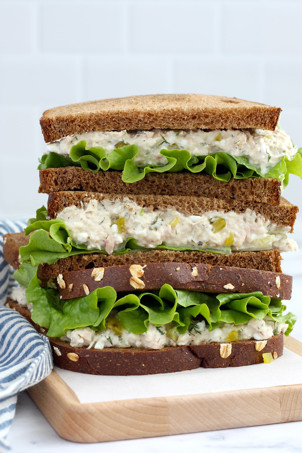 A tuna salad sandwich on rye bread, cut in half and stacked up on a wooden cutting board.