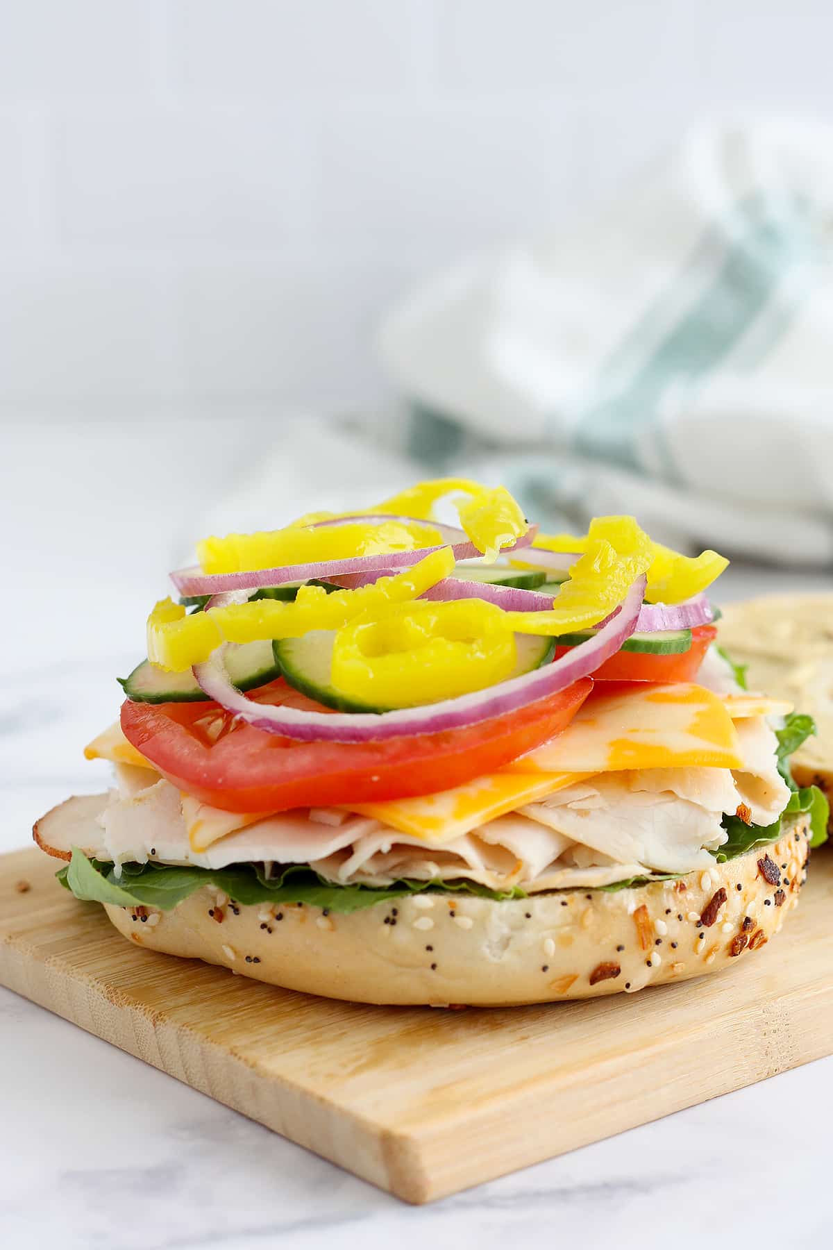 Half of a bagel topped with lettuce, turkey, cheese, and vegetables on a wooden cutting board.
