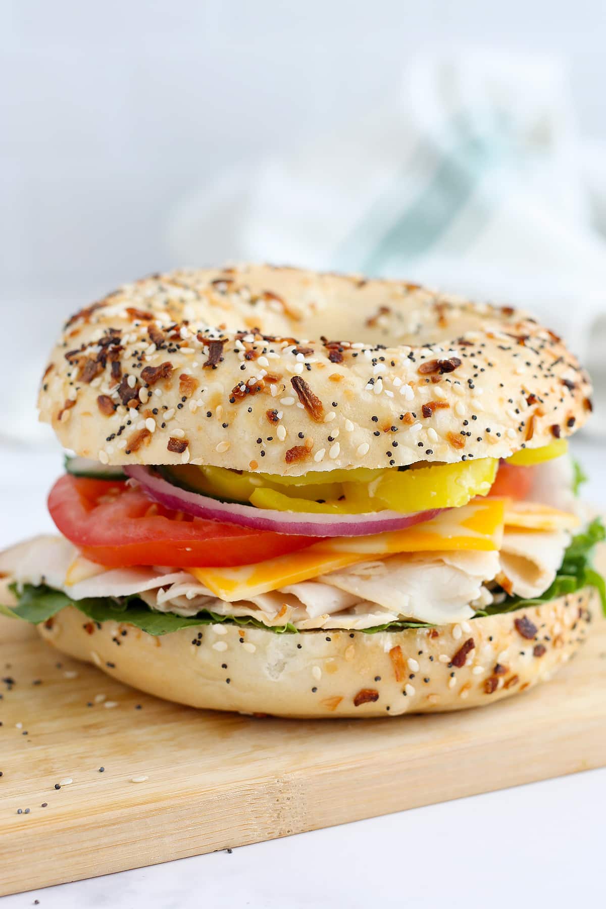 A turkey sandwich on an everything bagel with tomatoes, banana peppers, and cheese.