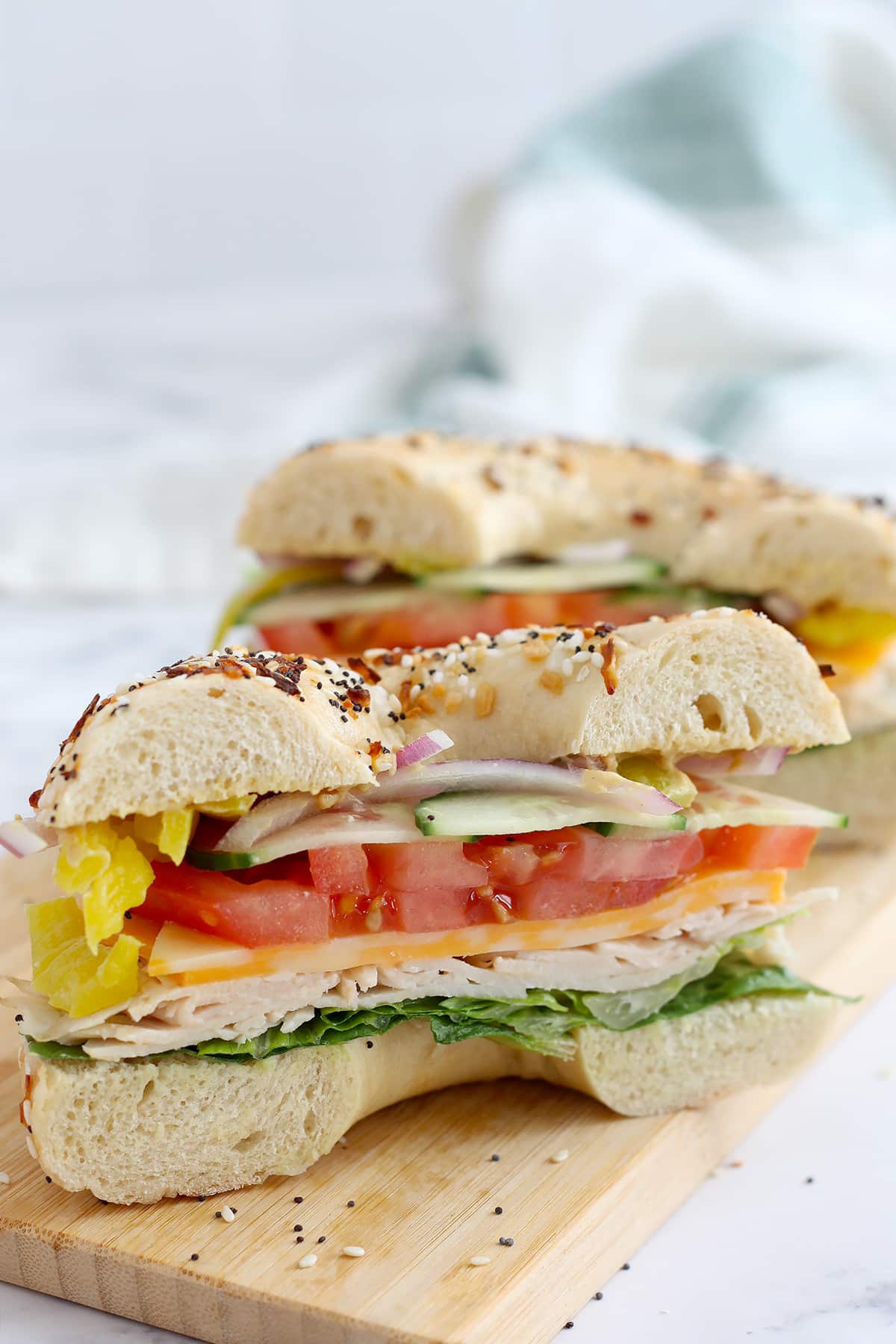 A turkey bagel sandwich with cheese and vegetables cut in half.