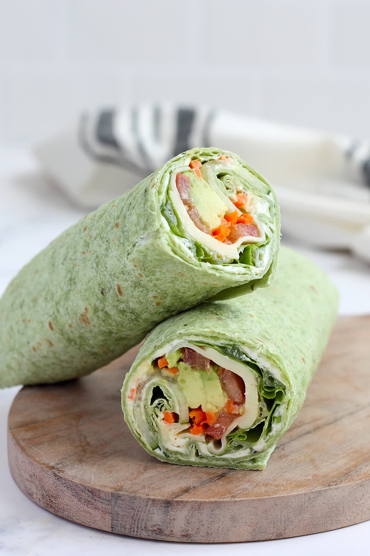 A veggie wrap in a spinach tortilla cut in half and placed on a wooden cutting board with a striped linen in the background.