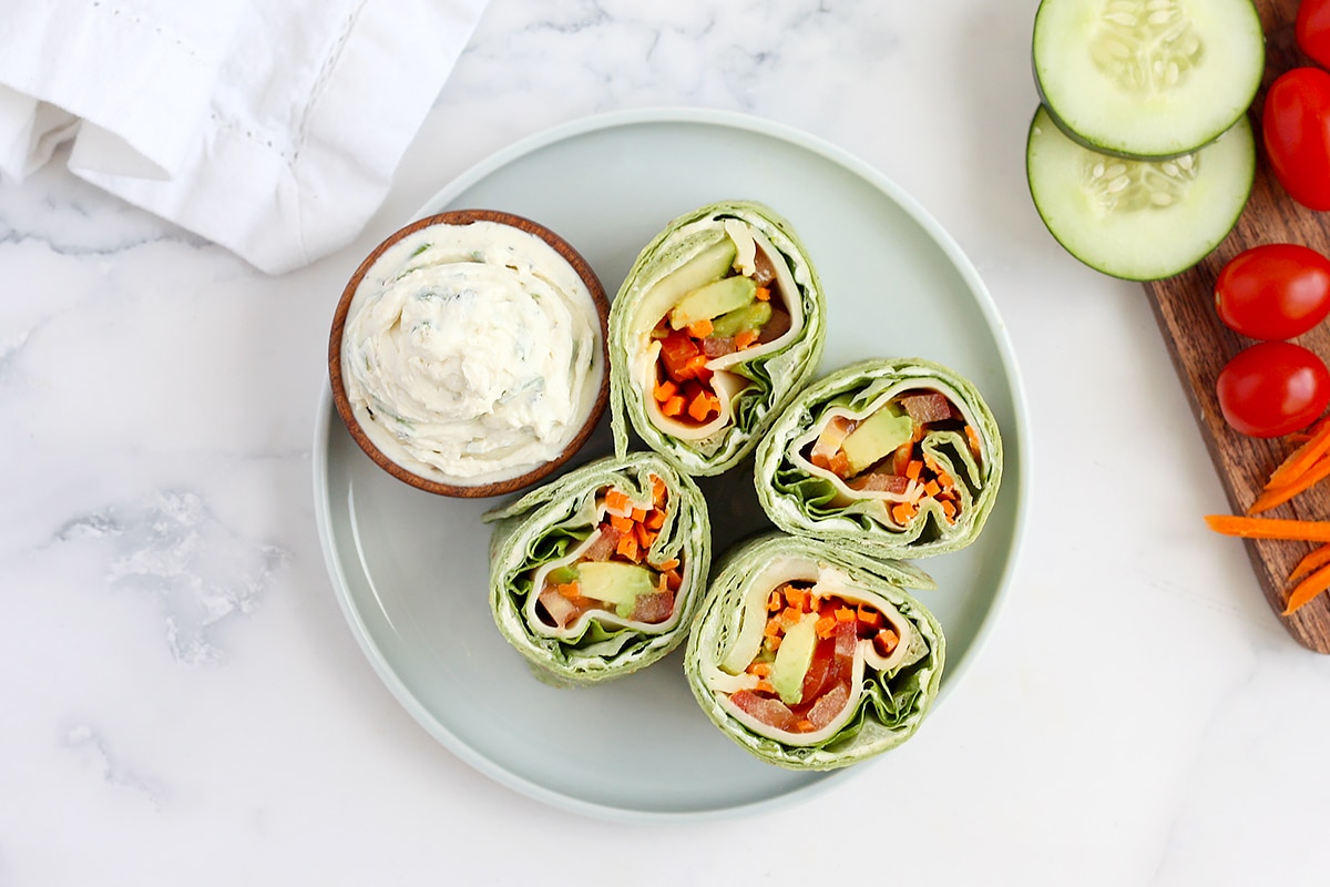 Veggie wraps sliced into pinwheels with fresh veggies in the background and a white linen.