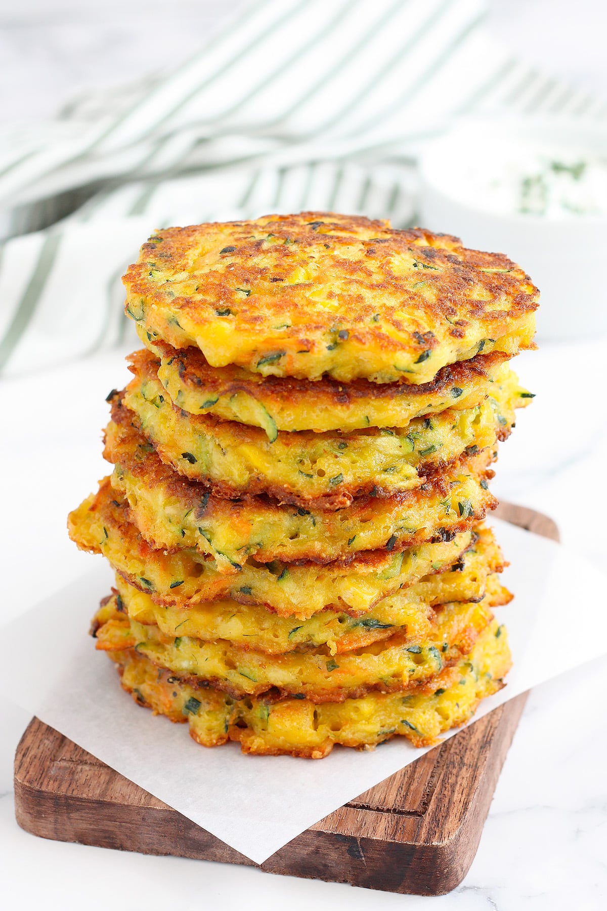 A stack of zucchini fritters on a wooden serving platter with a striped linen in the background.