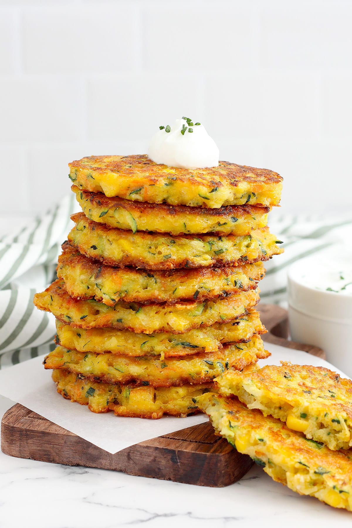 A close up shot of a stack of zucchini fritters with a bowl of chive sour cream.
