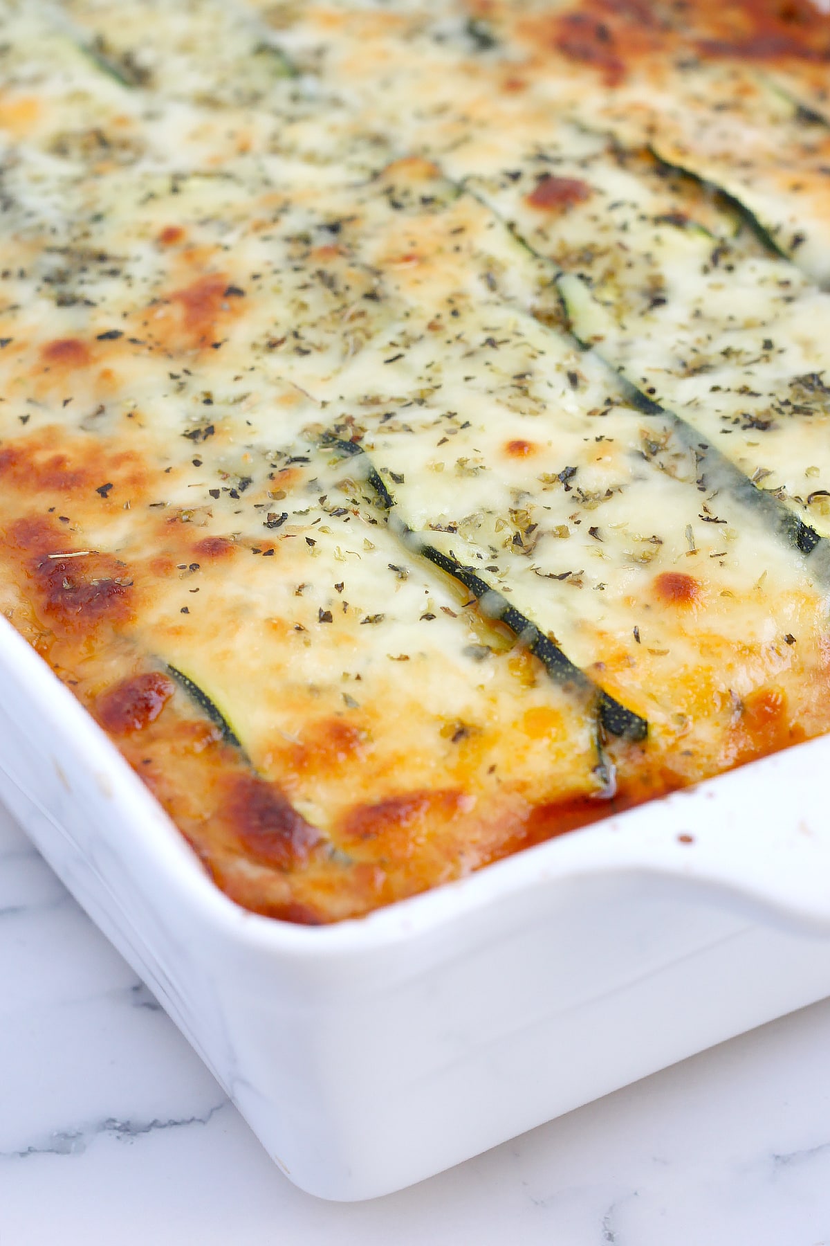 A close up shot of cheesy zucchini lasagna topped with dried basil and oregano.