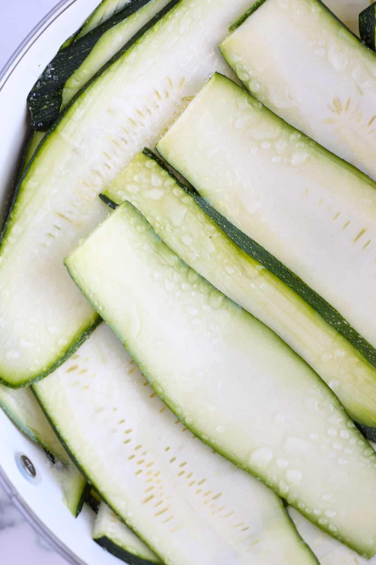 Slices of zucchini sweating in a metal colander.