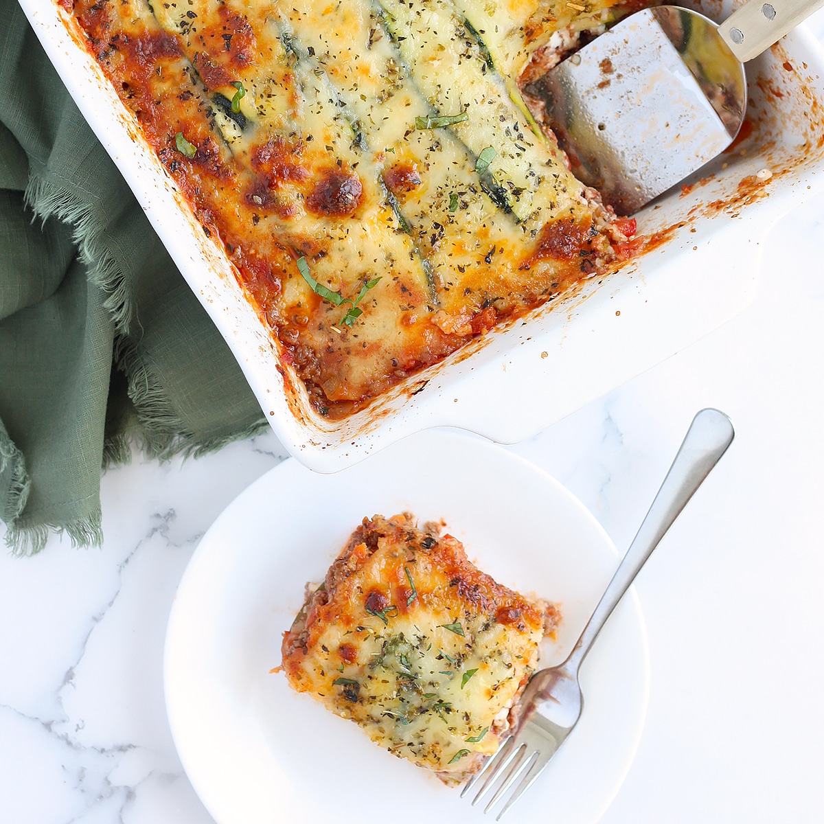 zucchini lasagna on a white plate with the full lasagna in a white 9x13 dish behind it