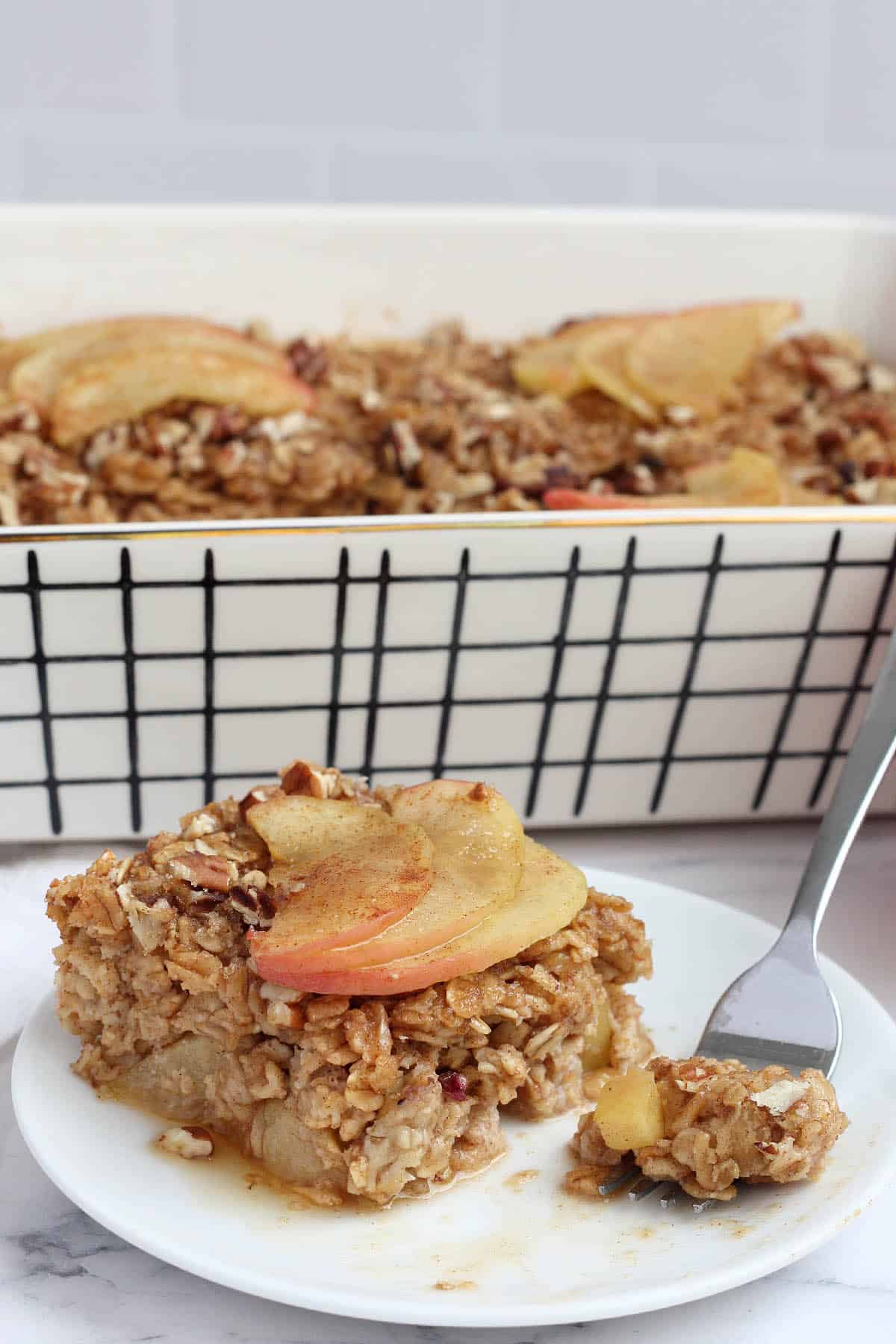 A serving of baked oatmeal topped with thinly sliced apples and cinnamon on a white plate.
