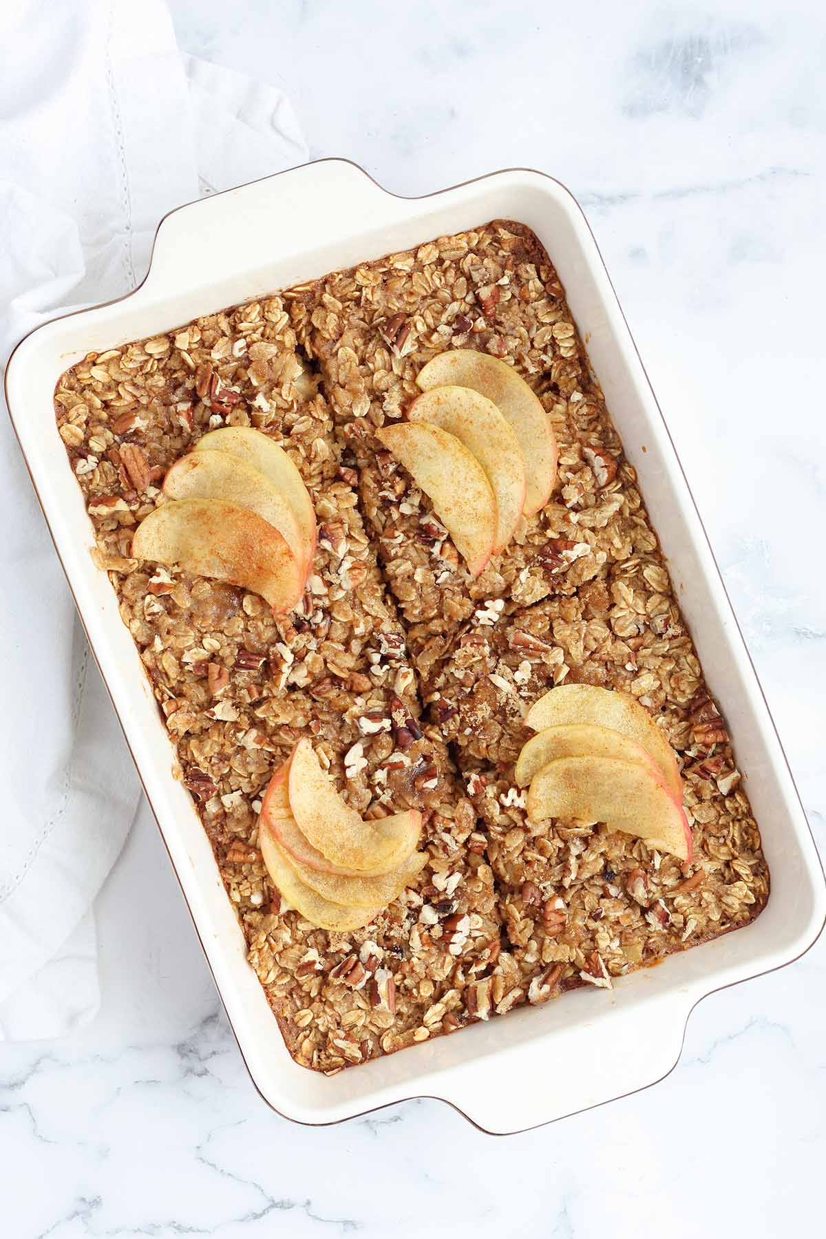 Apple Cinnamon Baked Oatmeal in a white ceramic serving dish topped with sliced apples and pecans.