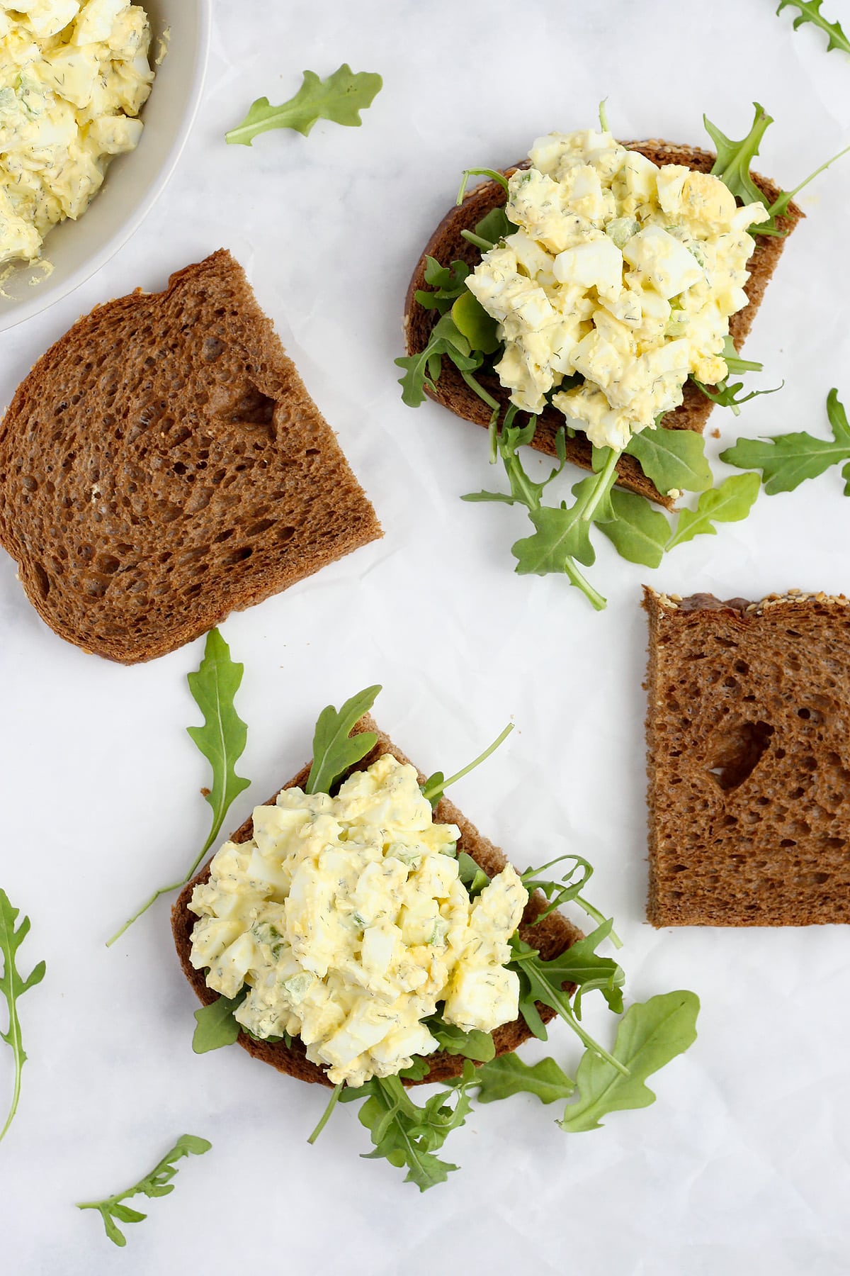 Slices of bread topped with arugula and homemade egg salad on a marble countertop.