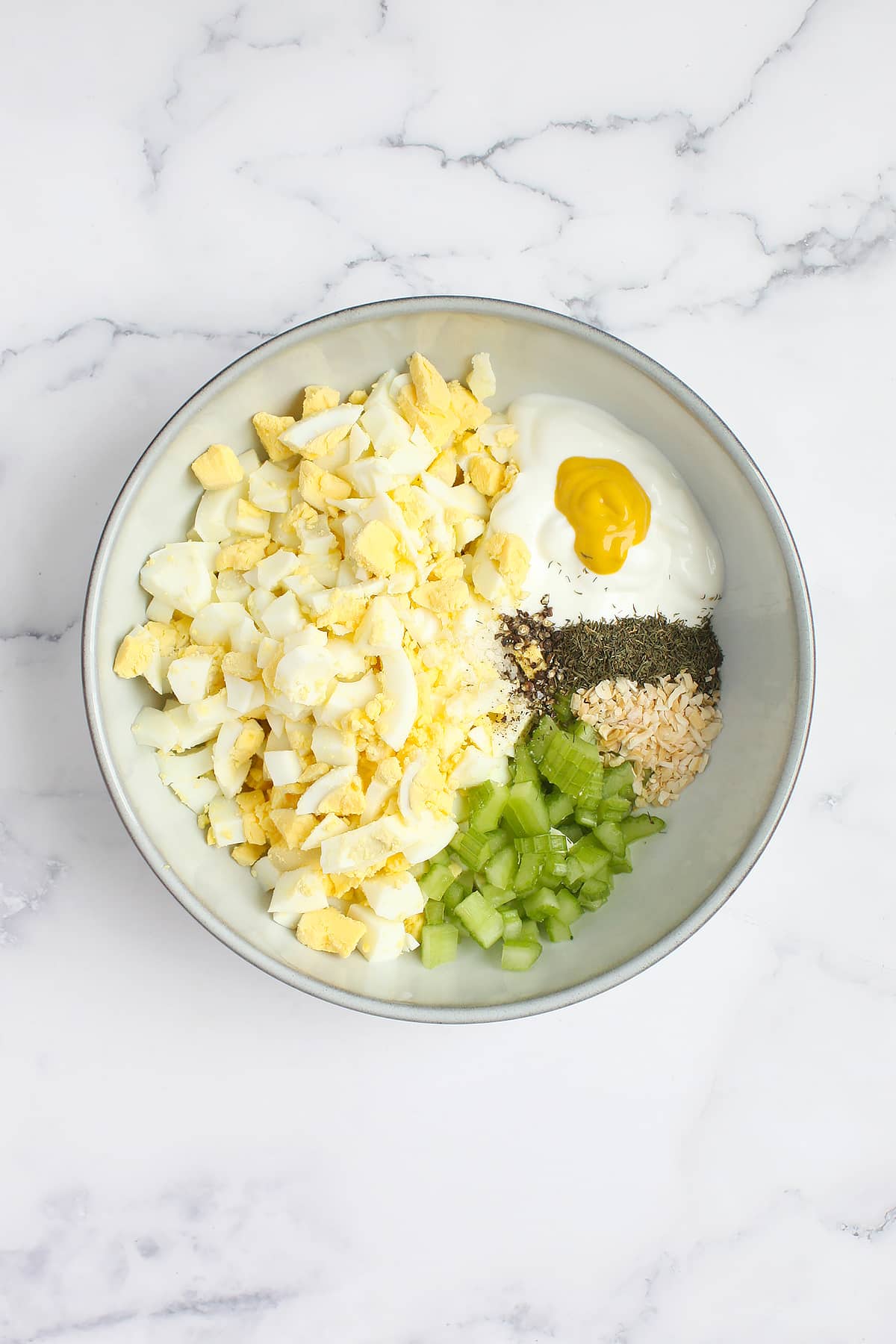 A mixing bowl with all of the ingredients for ،memade egg salad.