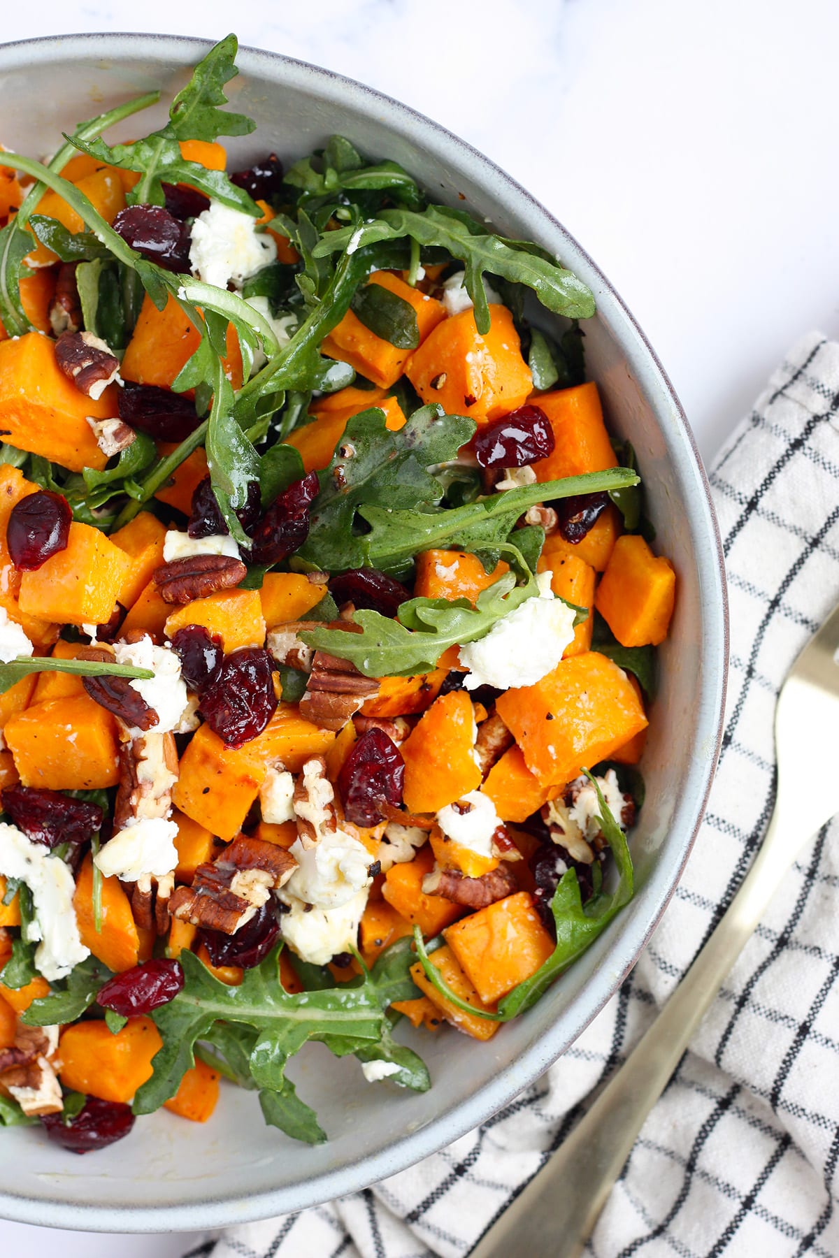 Roasted sweet potatoes, arugula, dried cranberries and goat cheese in a ceramic serving bowl.
