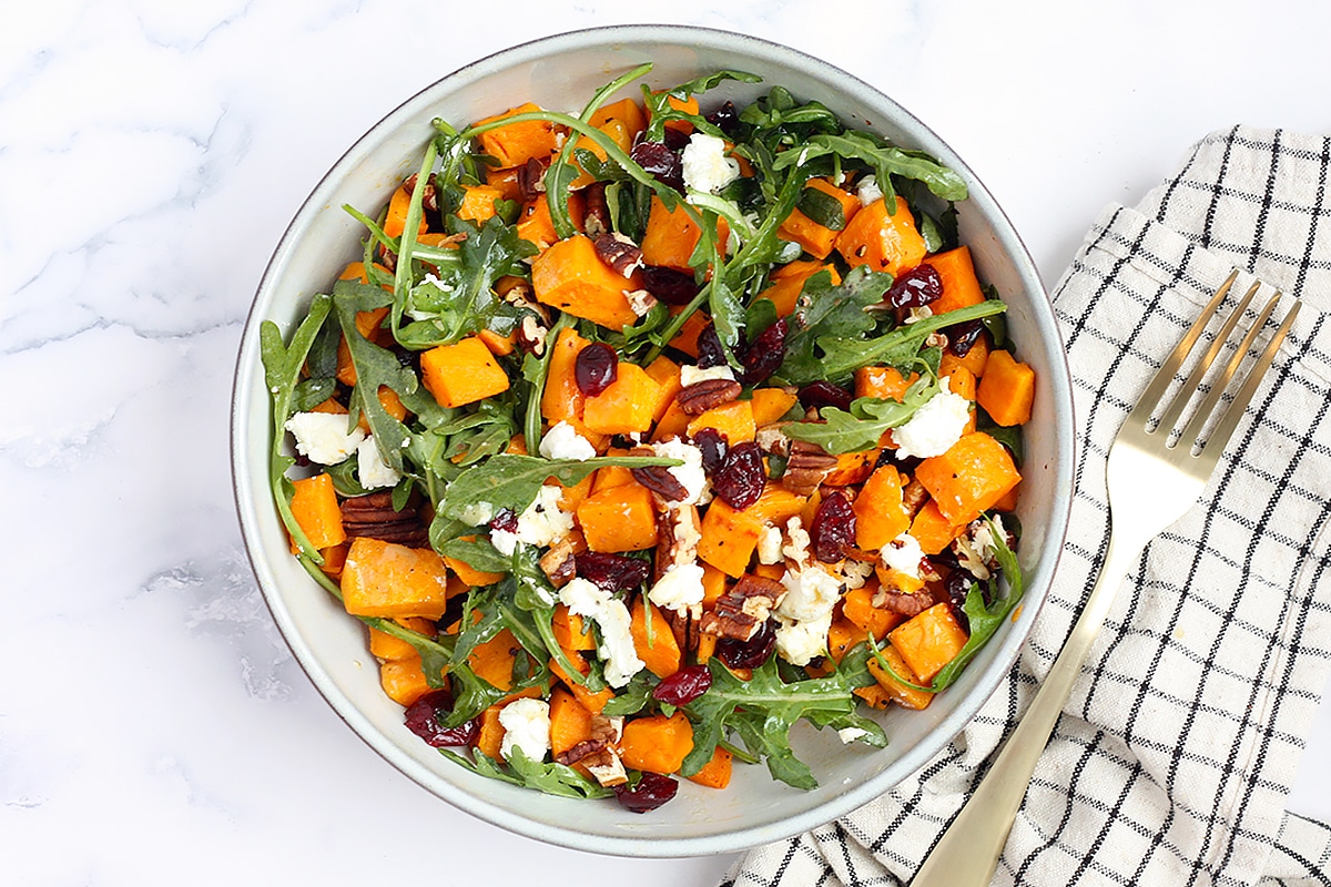 An overhead shot of arugula salad with sweet potatoes, dried cranberries, and crumbled goat cheese.