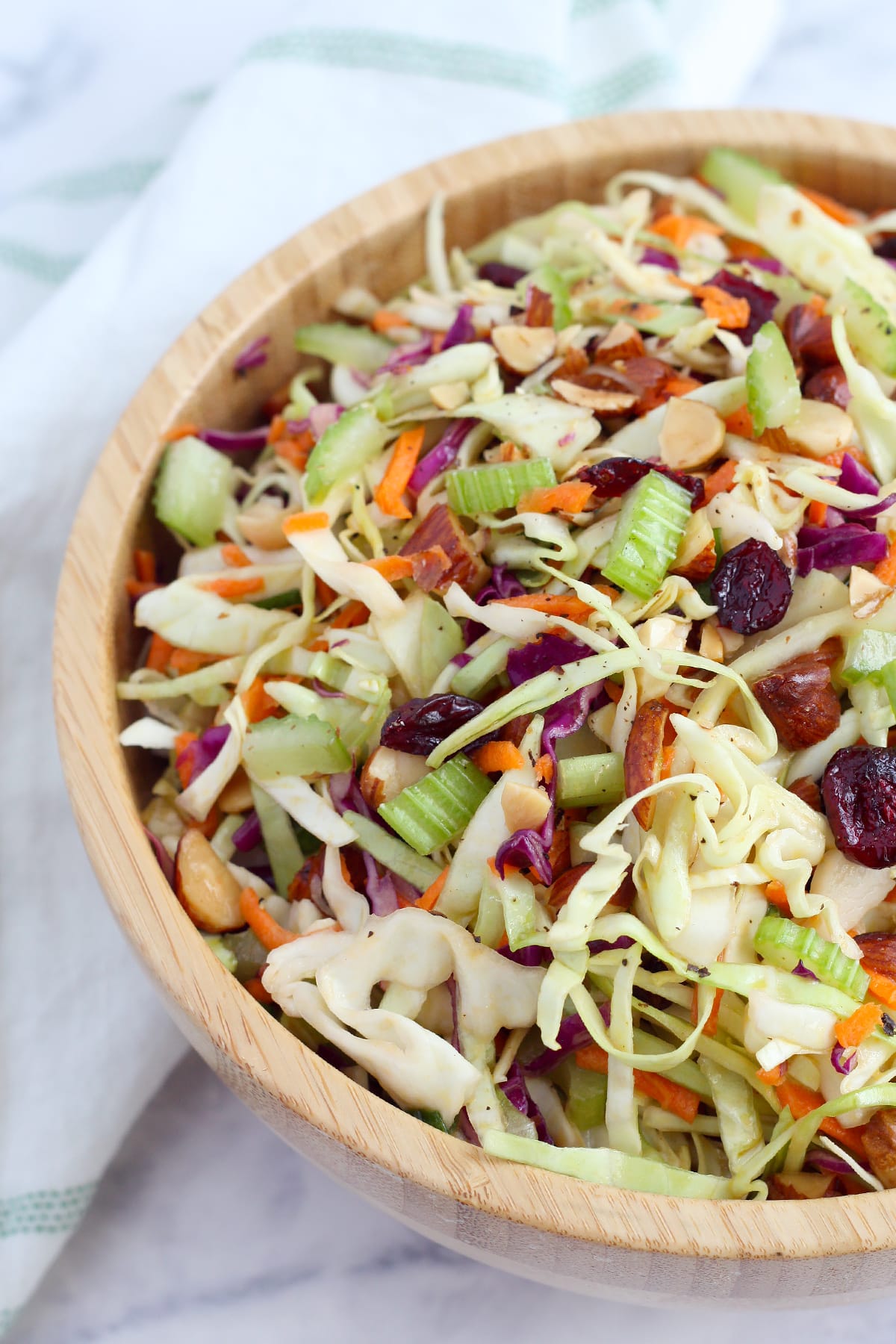 Homemade coleslaw with celery and dried cranberries in a wooden serving bowl.