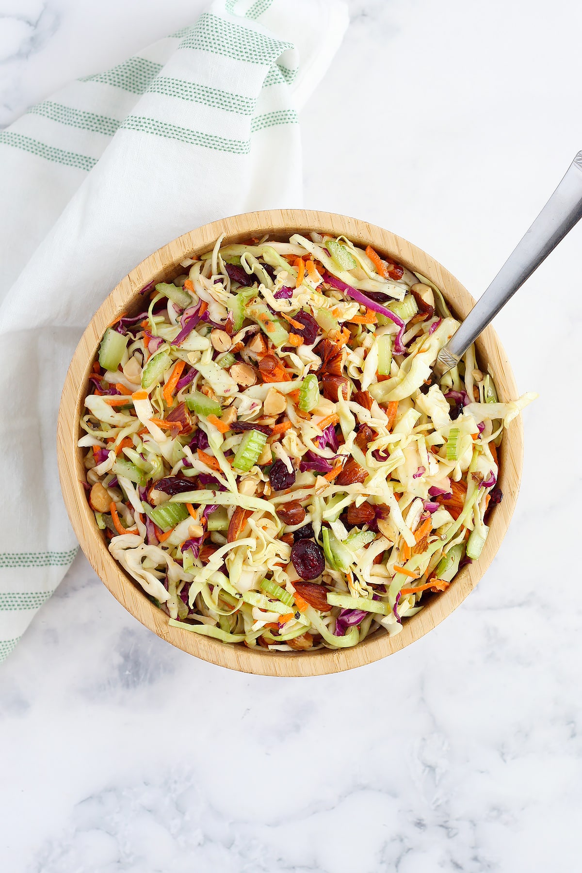 An overhead shot of smoky almond coleslaw in a wooden serving bowl with a silver spoon.