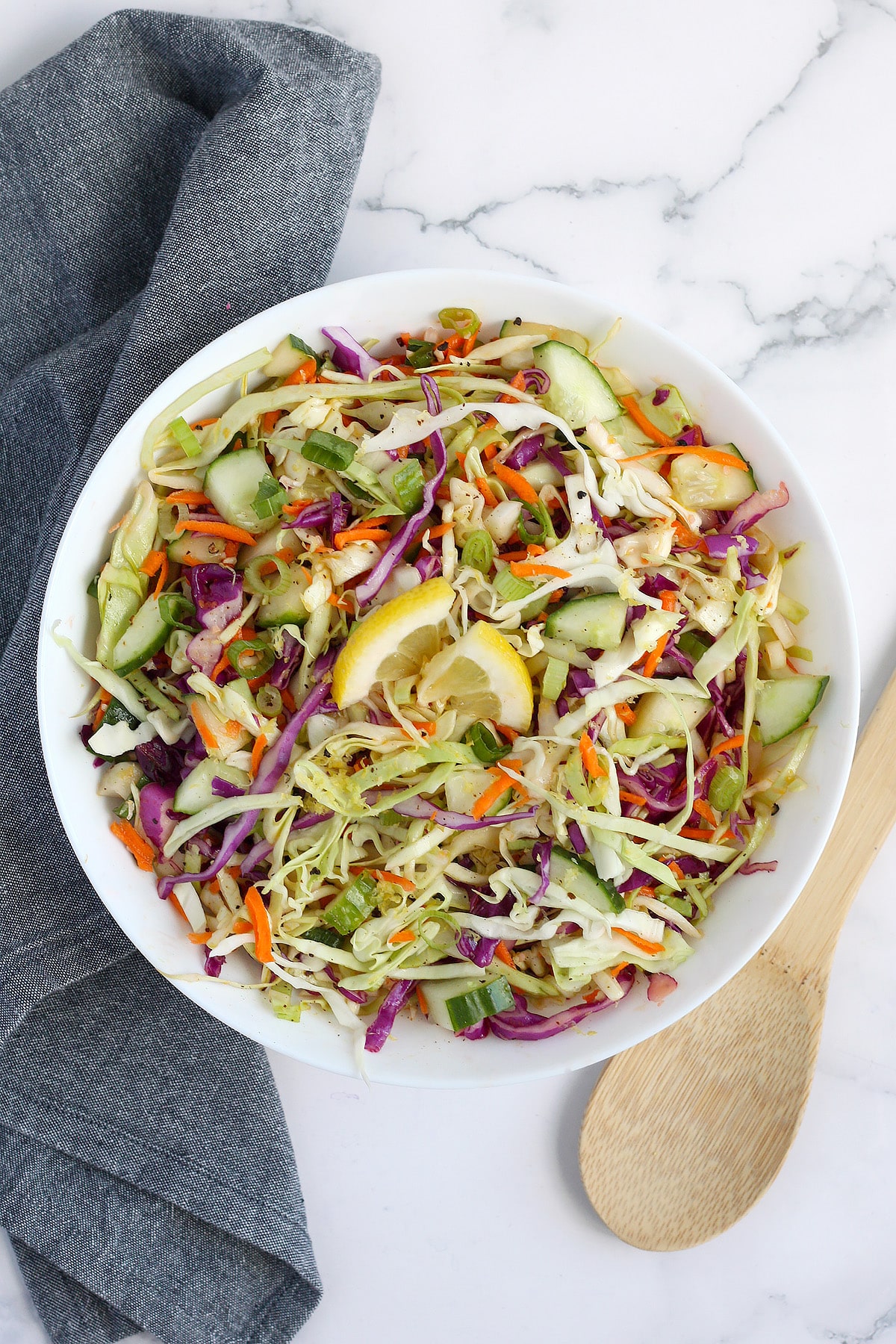 Coleslaw with cucumbers and garnished with lemon slices in a serving bowl.