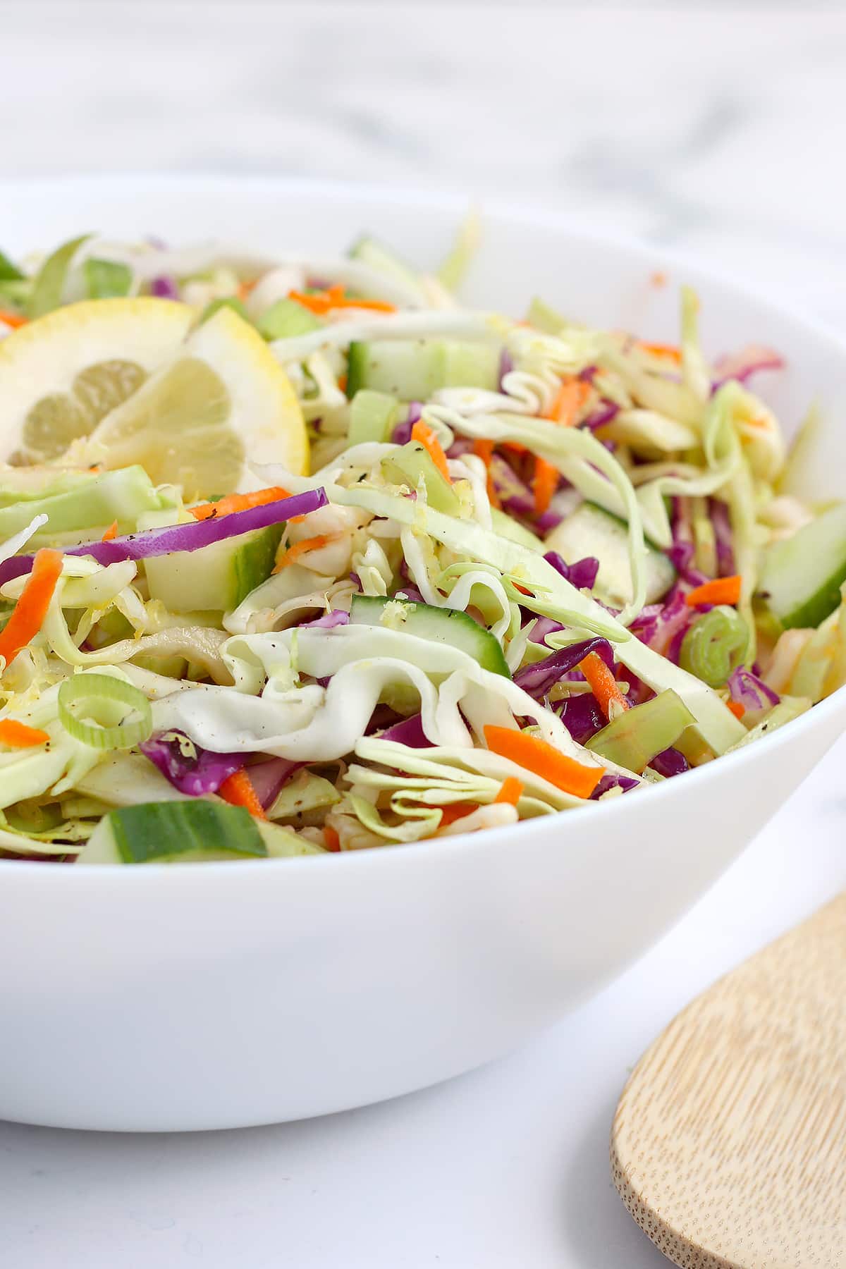 A close up shot of homemade coleslaw topped with lemon slices in a white serving bowl.