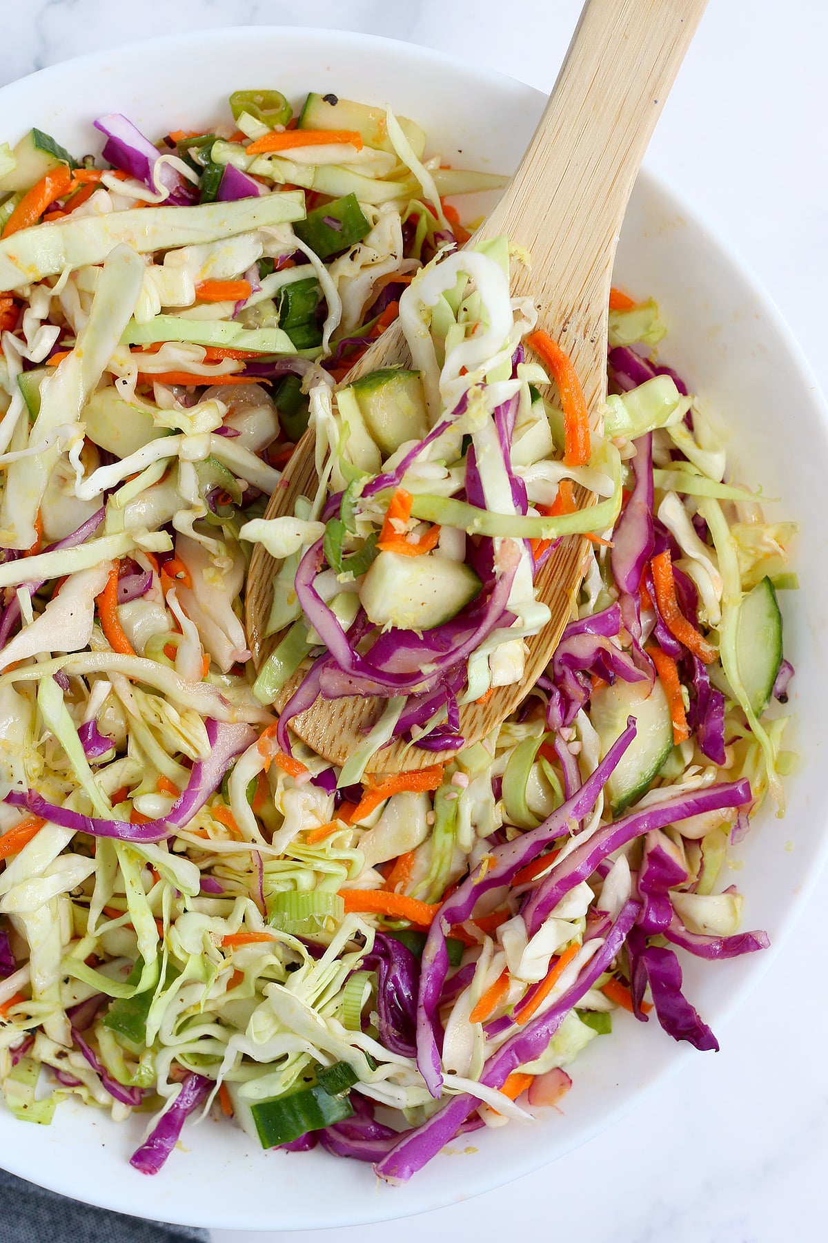 Mayo-free coleslaw in a white bowl with a wooden serving spoon.