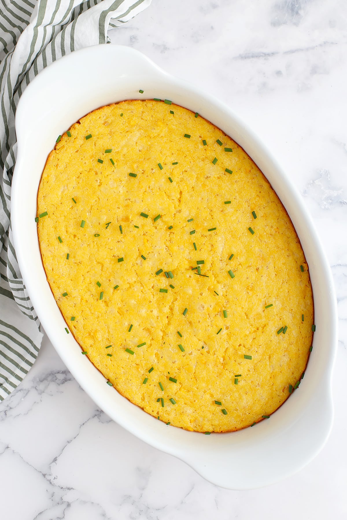 Cornbread casserole baked in an oval white ceramic serving dish and topped with minced chives.