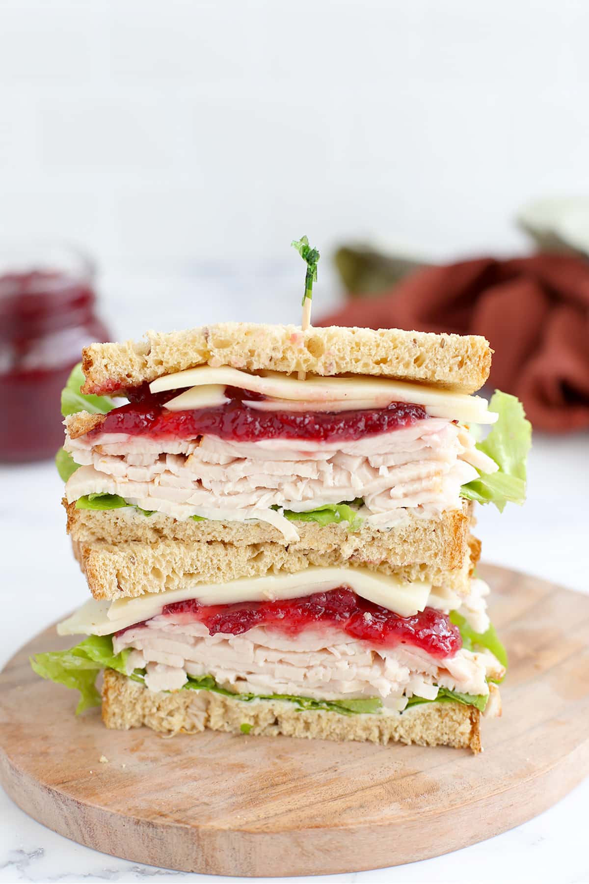 A turkey cranberry sandwich on wheat bread, cut in half and stacked on a wooden cutting board.