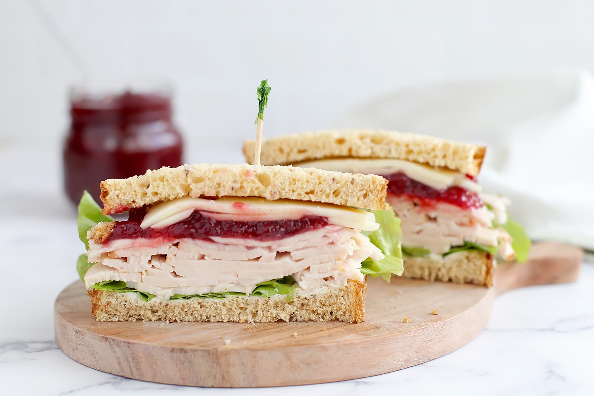 A turkey, cheese, lettuce and cranberry sauce sandwich sliced in half and topped with a toothpick.