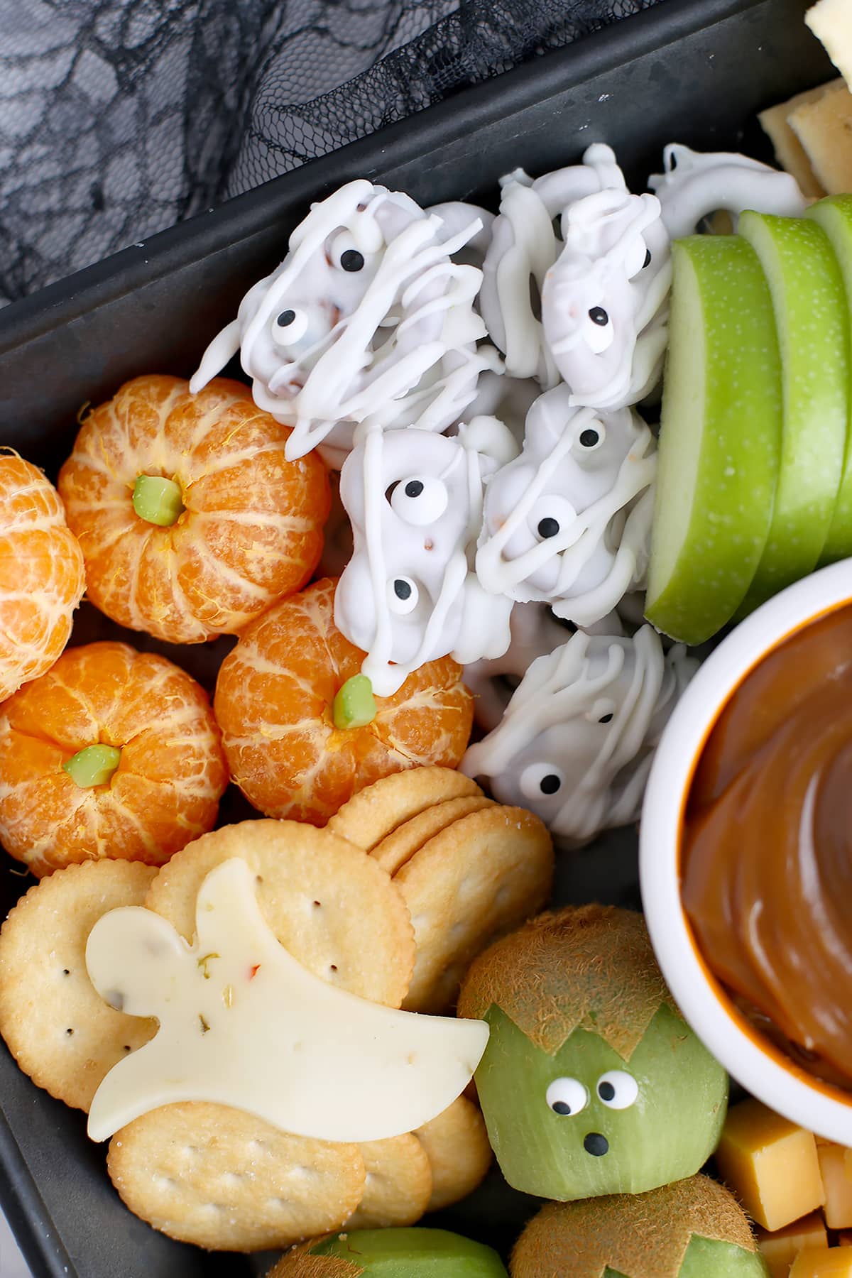 White chocolate pretzel mummies, sliced apples, and mandarin oranges peeled and decorated with a celery stalk to resemble a pumpkin.