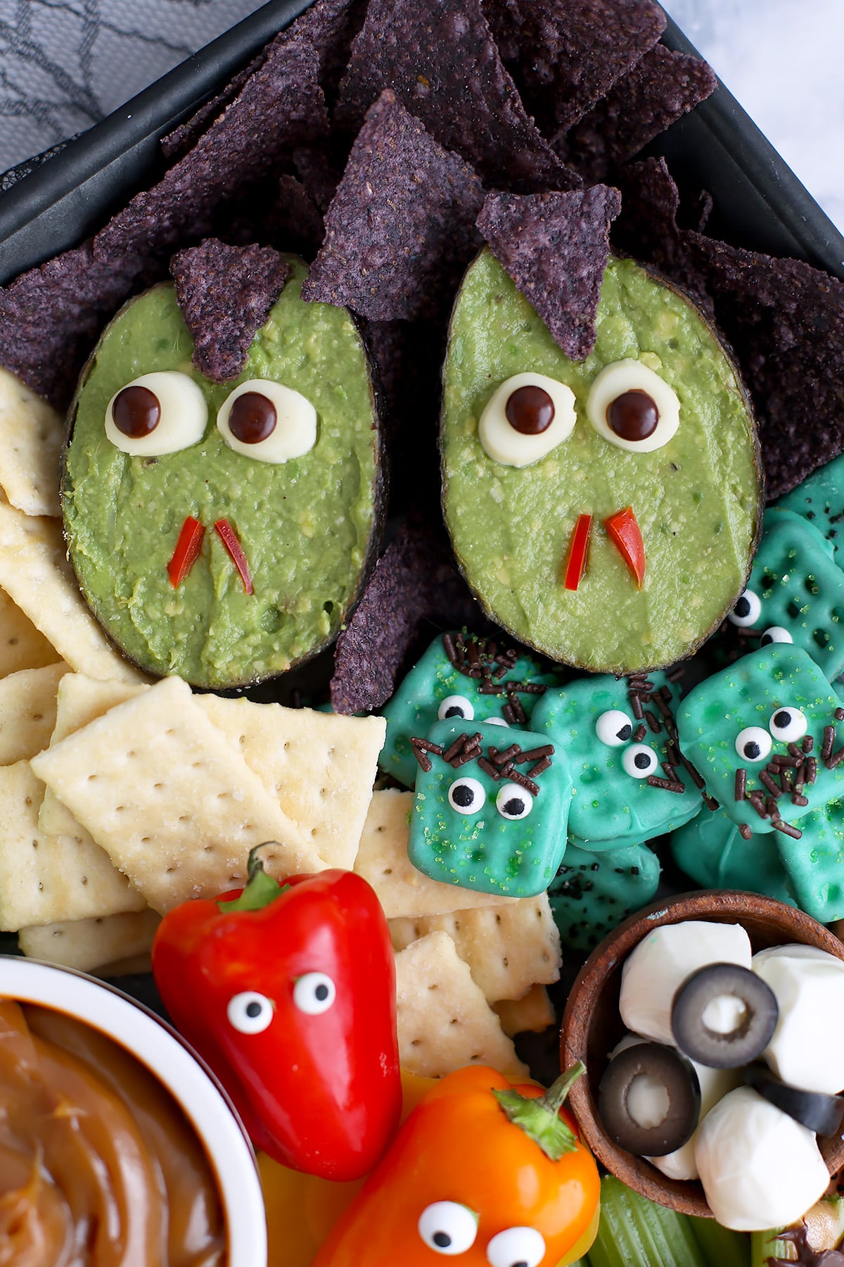 Two avocado shells filled with guacamole and decorated to look like vampires and other assorted snack foods.