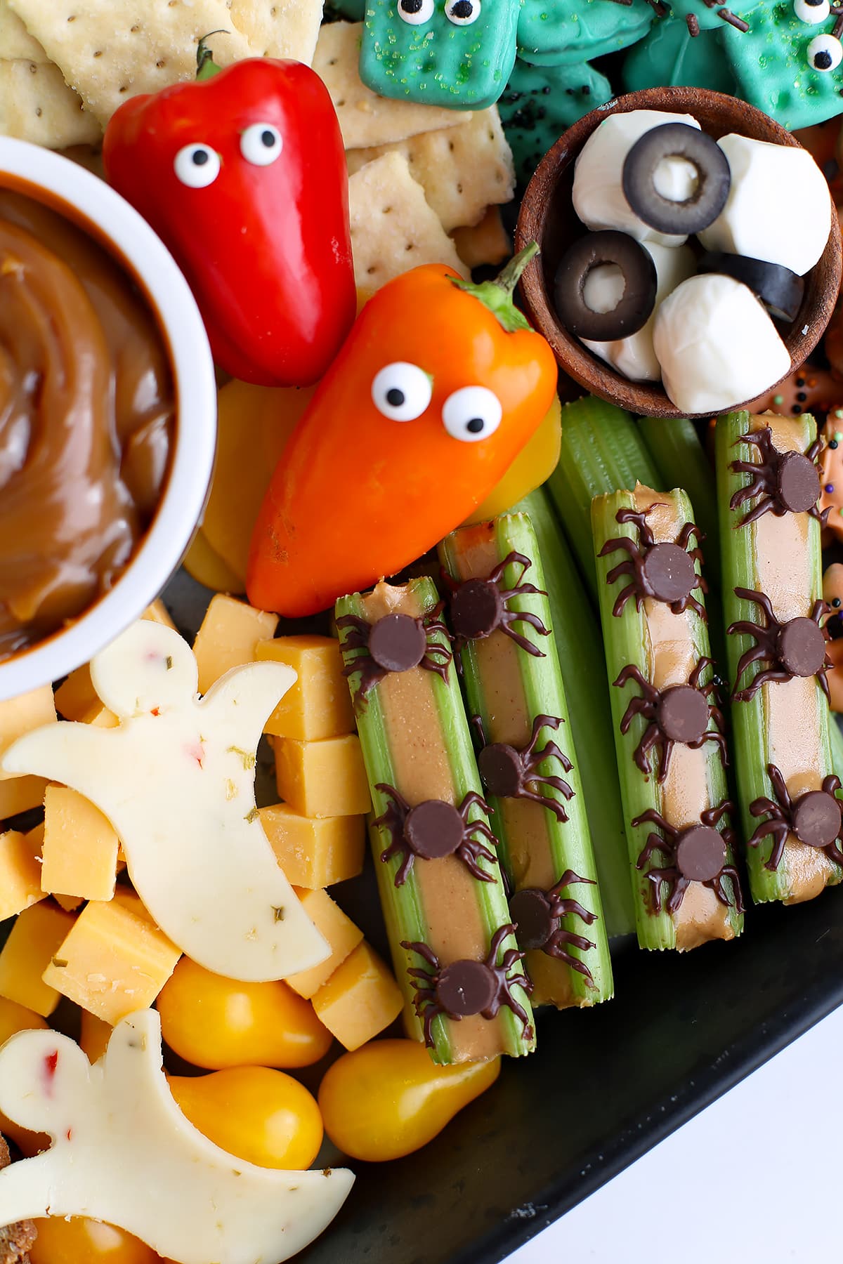 Mini bell peppers with candy eyes, crackers, celery sticks with peanut butter, and cheese slice ghosts on a snack tray.