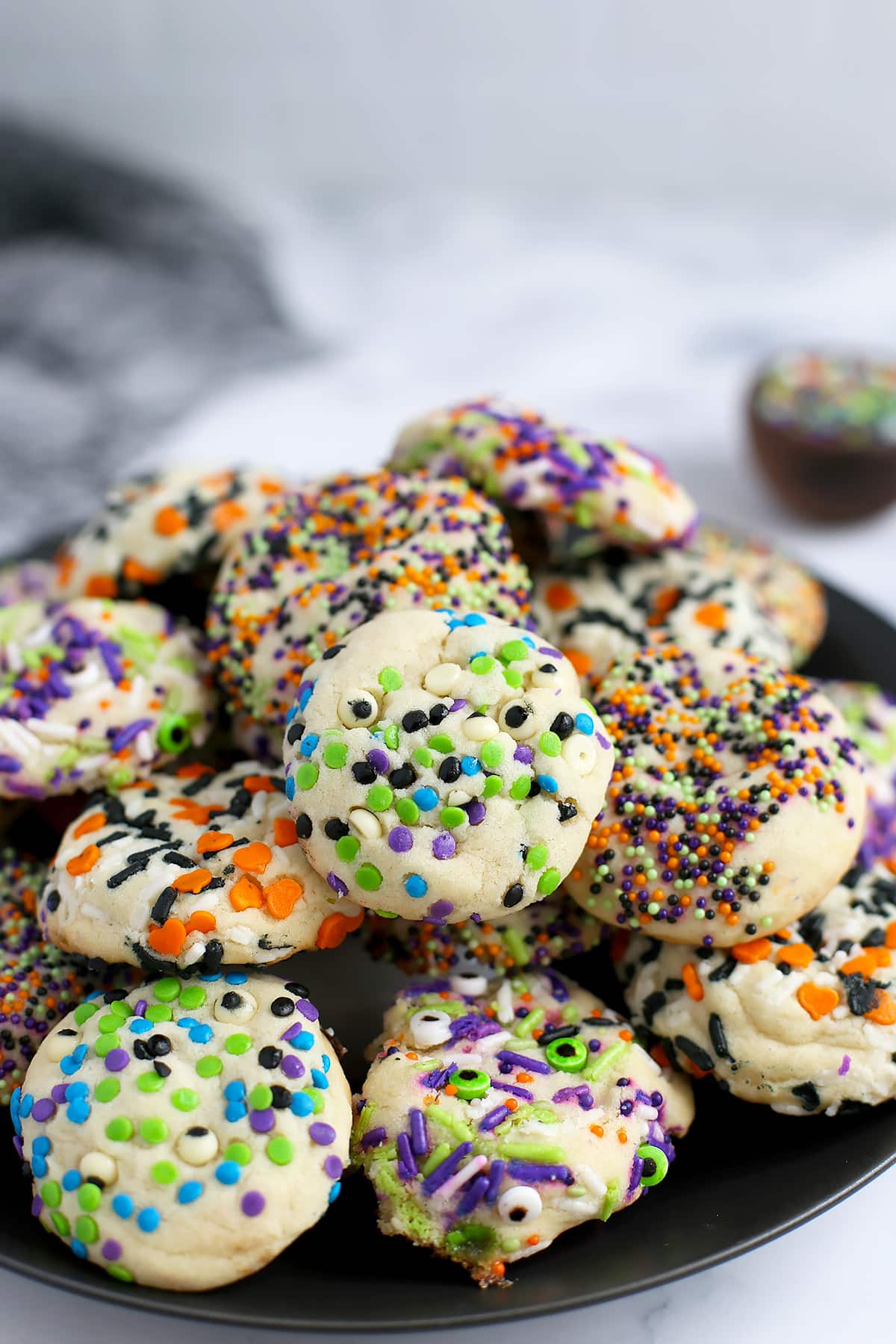 A stack of soft and chewy sugar cookies rolled in halloween sprinkles on a black ceramic serving plate.