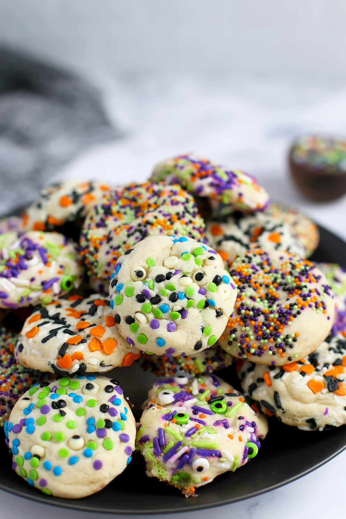 A stack of soft and chewy sugar cookies rolled in halloween sprinkles on a black ceramic serving plate. 