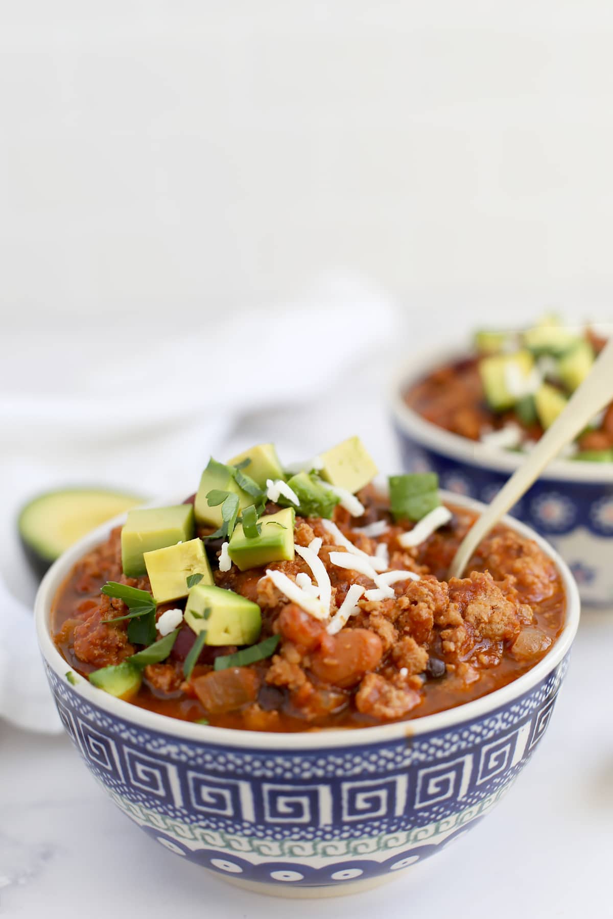 A blue and white ceramic bowl filled with turkey chili and topped with cilantro and avocado.