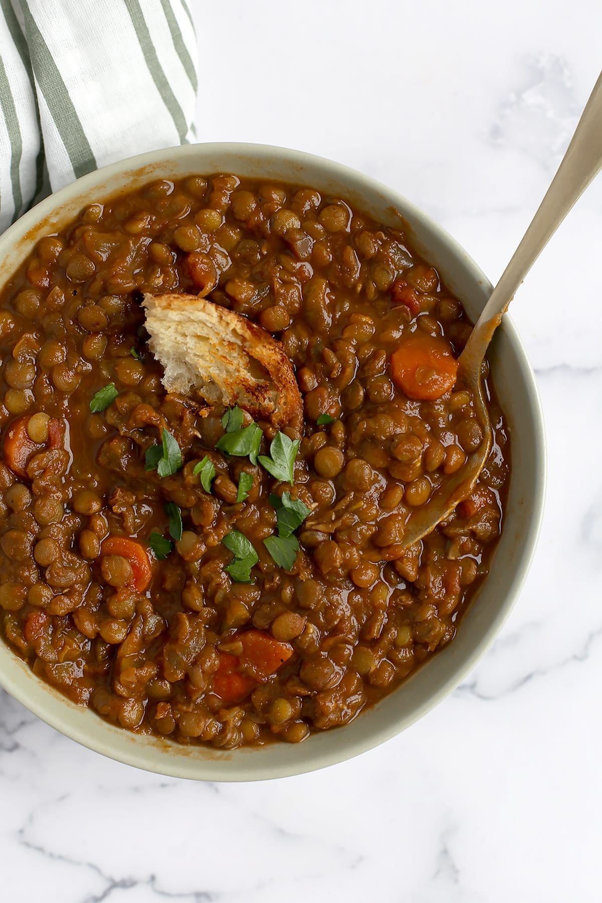 A bowl of hearty lentil soup topped with fresh parsley and a crust of bread with a spoon in it.