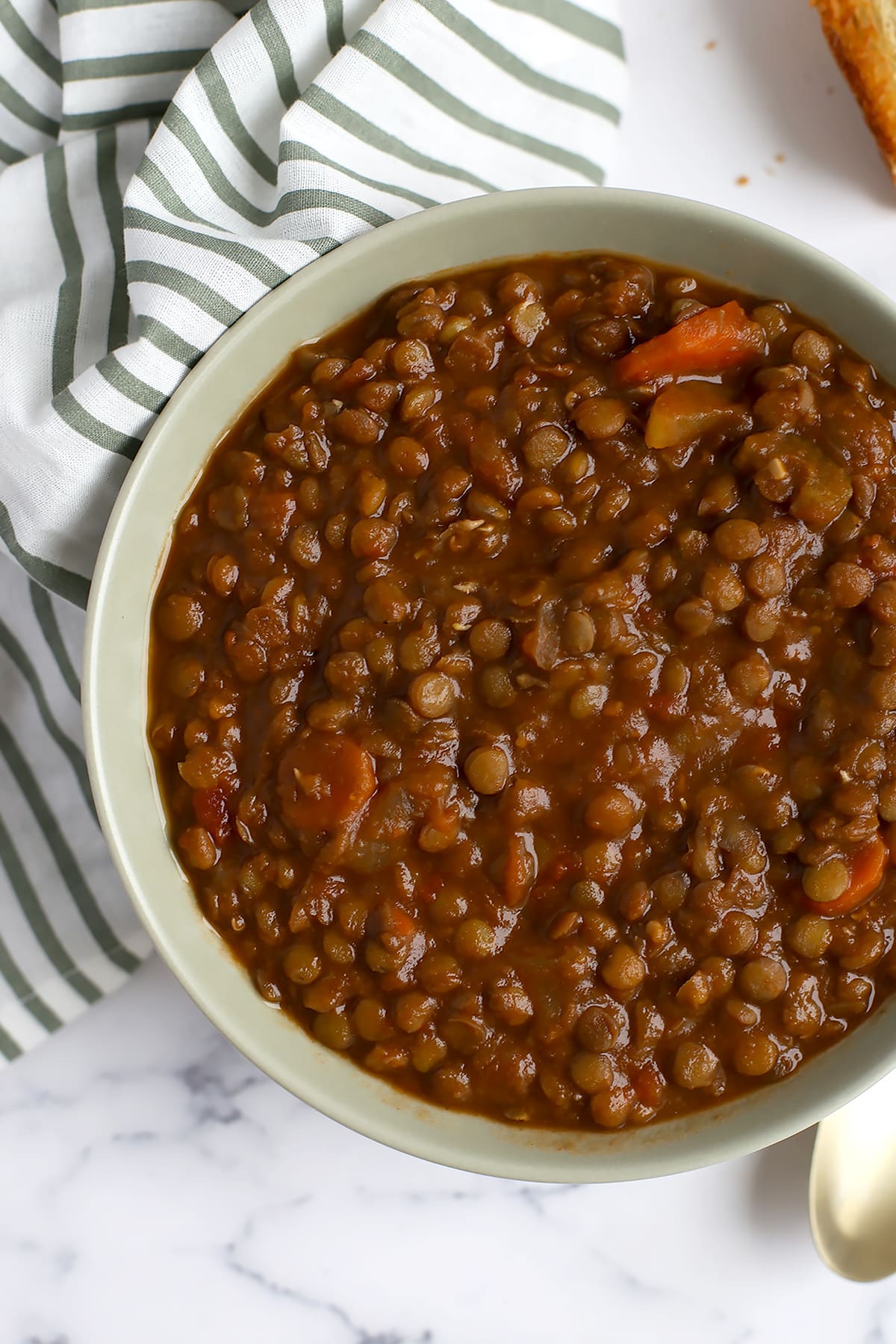 Homemade lentil soup in a gray serving bowl with a striped linen in the background.